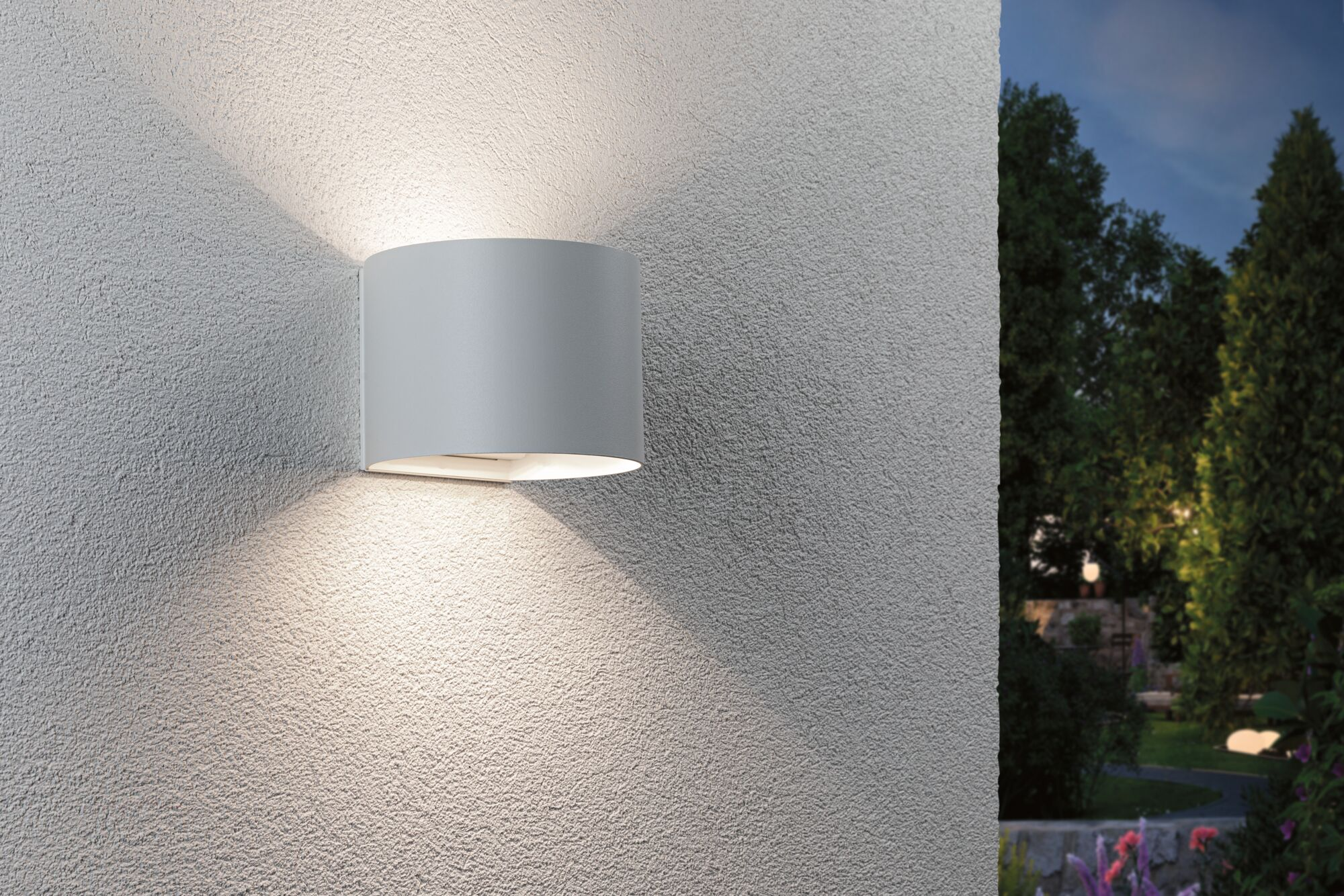 Eine graue zylindrische Wandleuchte strahlt Licht nach oben und unten an eine verputzte Wand.