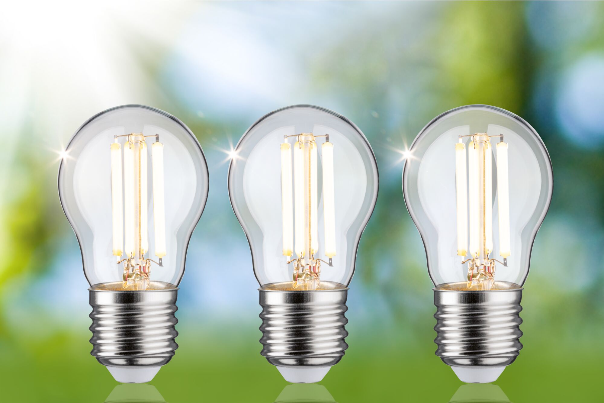 Drei beleuchtete LED-Glühbirnen mit sichtbaren Filamenten stehen vor einem verschwommenen grünen Hintergrund.