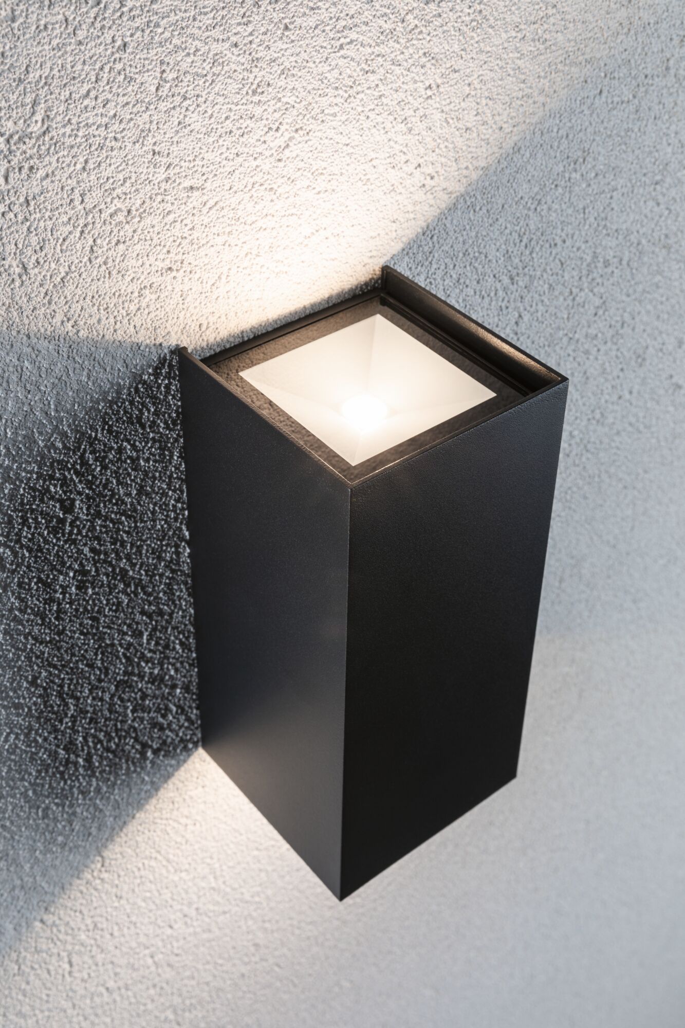Eine schwarze, rechteckige Wandlampe an einer strukturierten grauen Wand, die Licht nach oben und unten wirft.