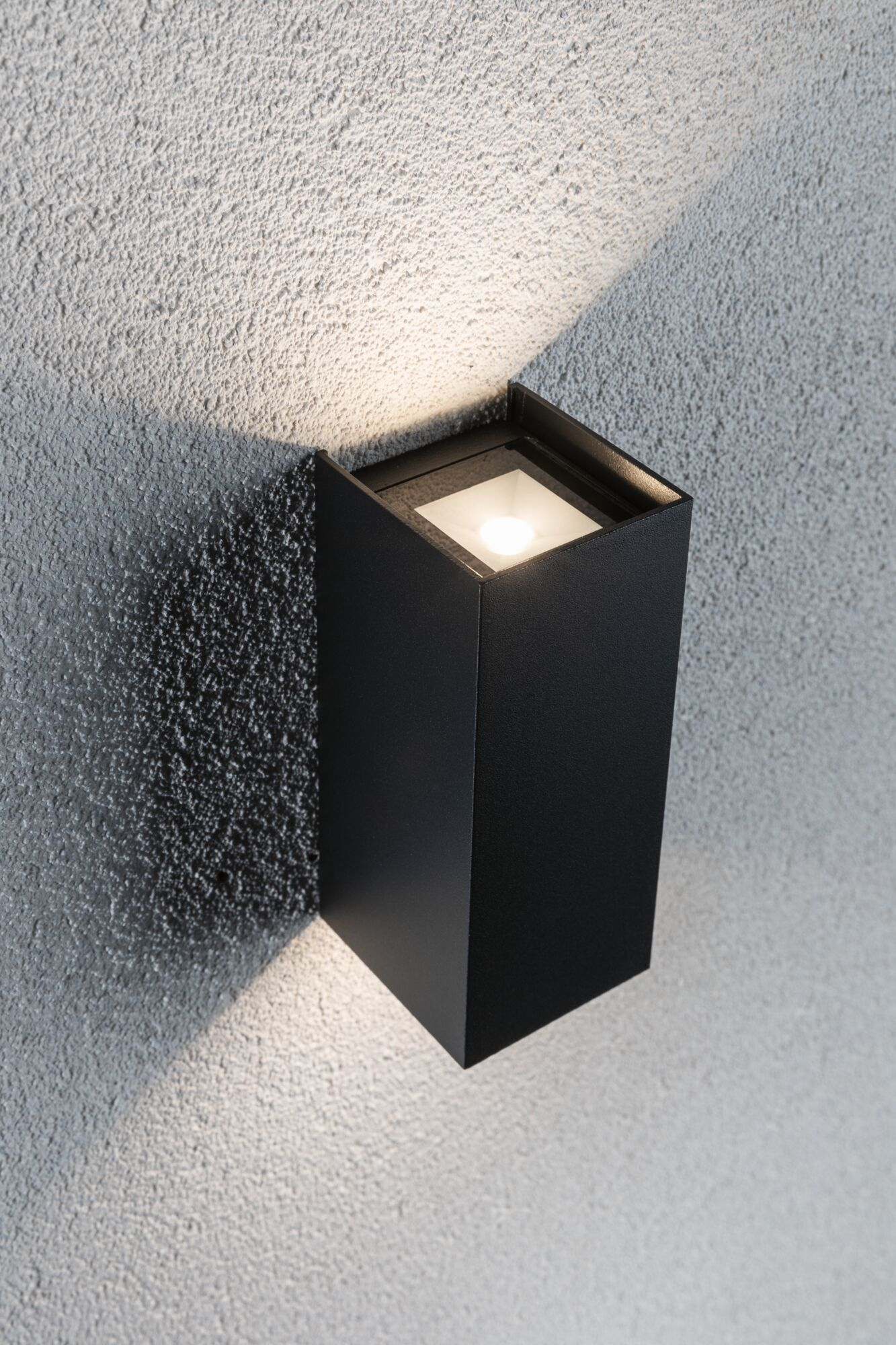 Eine schwarze Wandleuchte an einer strukturierten grauen Wand strahlt Licht nach oben und unten aus.