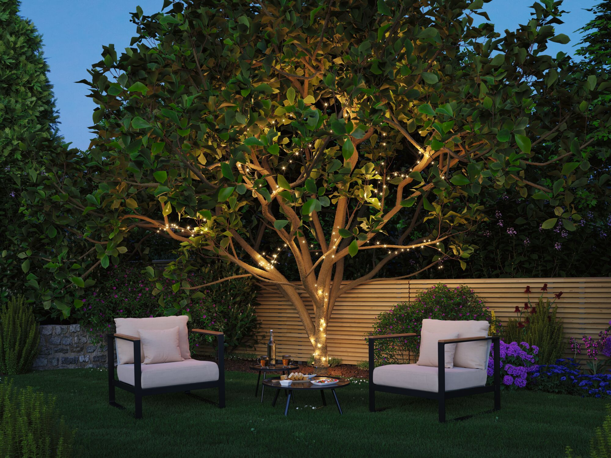 Zwei Sessel und Kaffeetische stehen nachts im Garten vor einem großen Baum mit Lichterkette.