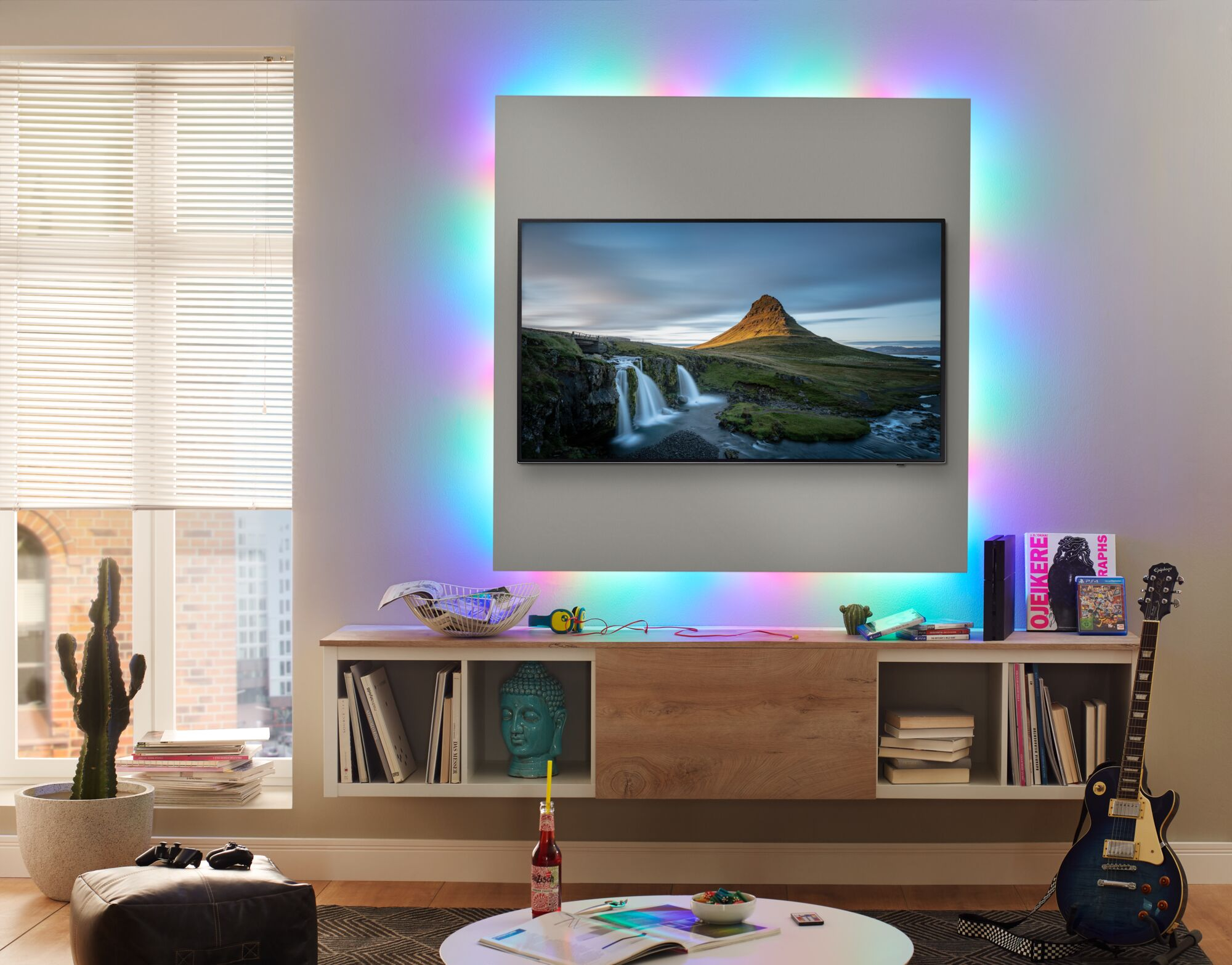 Wohnzimmer mit wandmontiertem Fernseher, bunter Hintergrundbeleuchtung, niedriger Holzkonsole und Akustikgitarre.