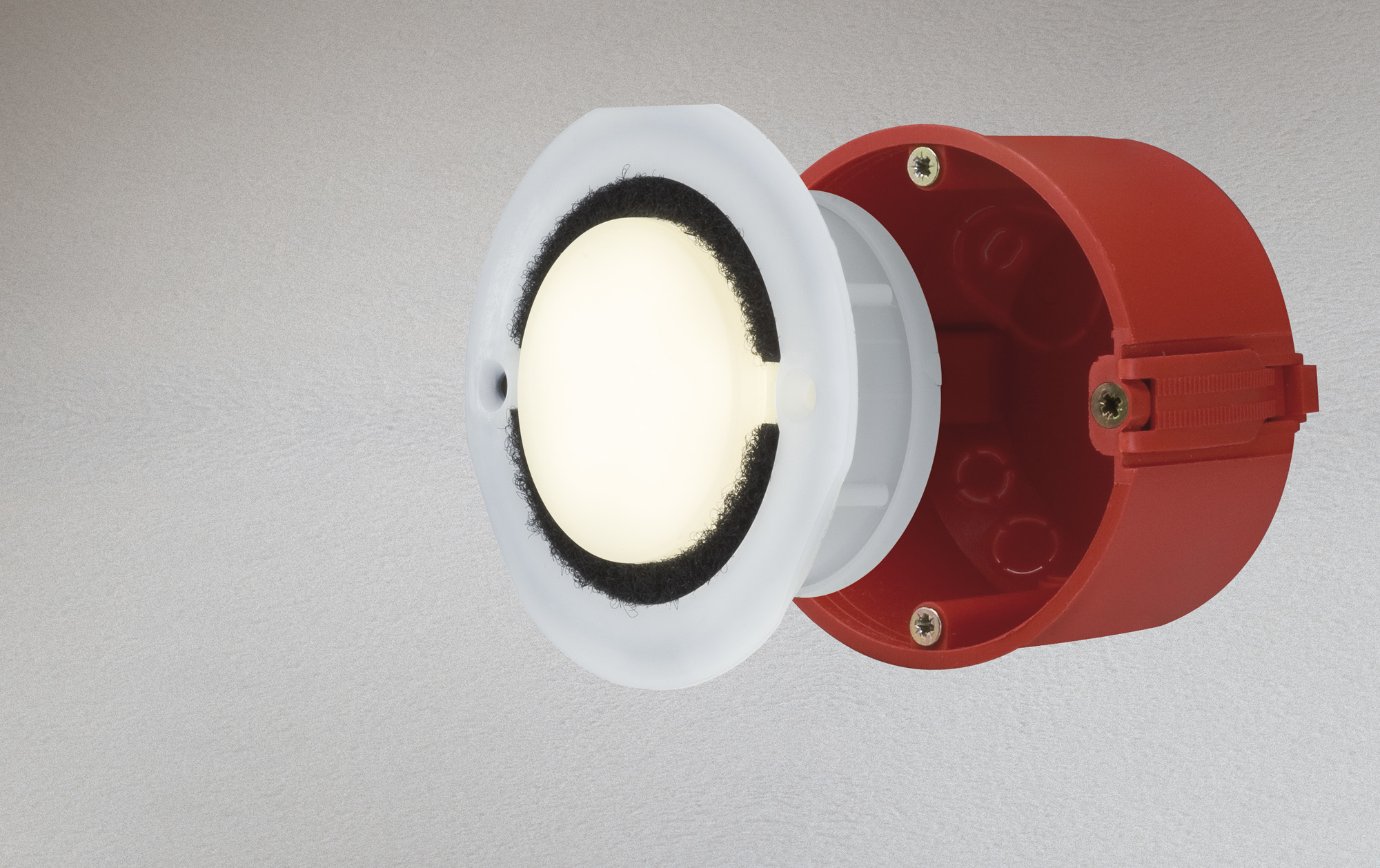 Eine weiße Lampe mit schwarzem Rand ist vor einer roten zylindrischen Wanddose montiert.