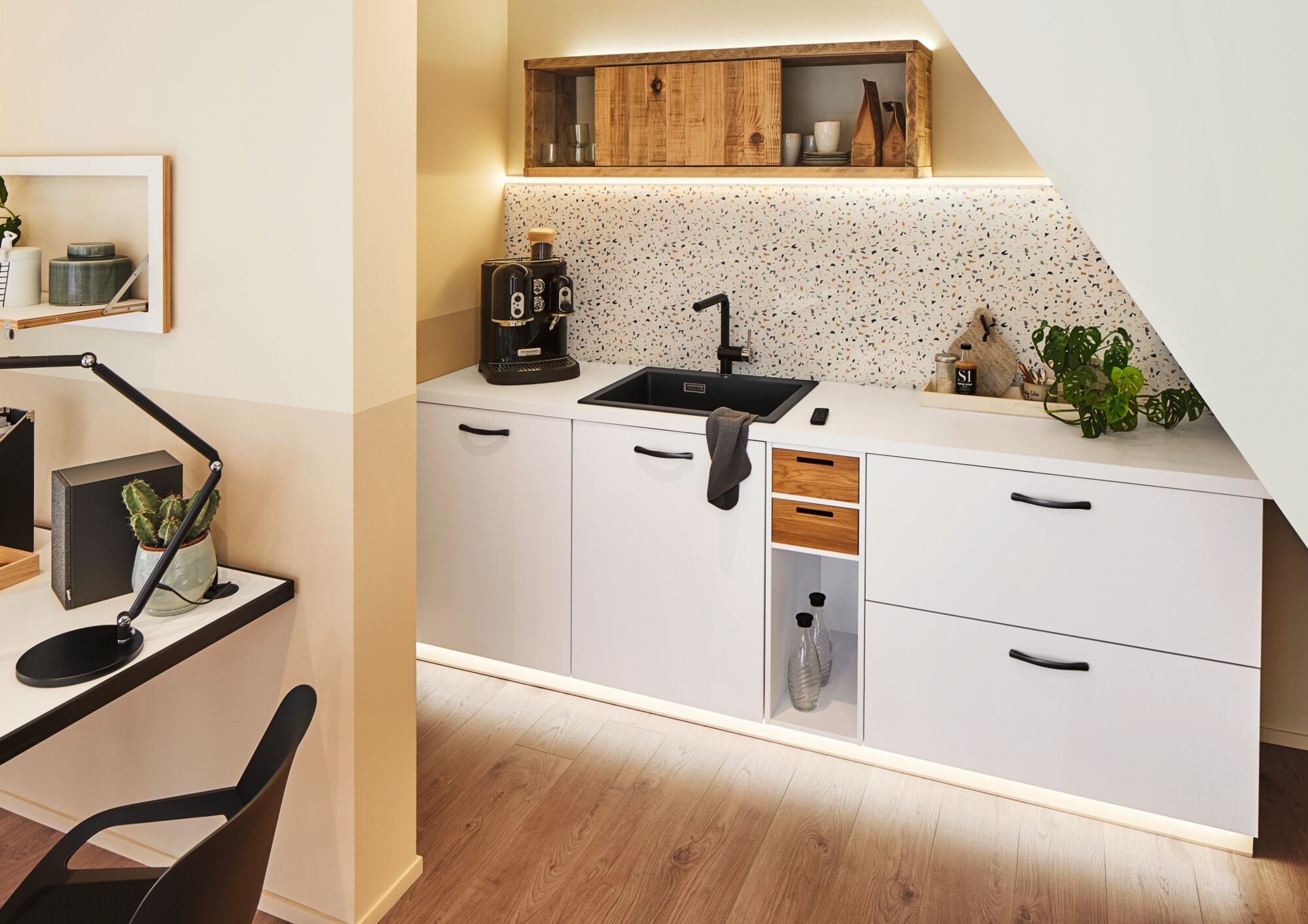 Moderne Küche mit weißen Schränken, schwarzem Waschbecken, Kaffeemaschine und Terrazzo-Rückwand.