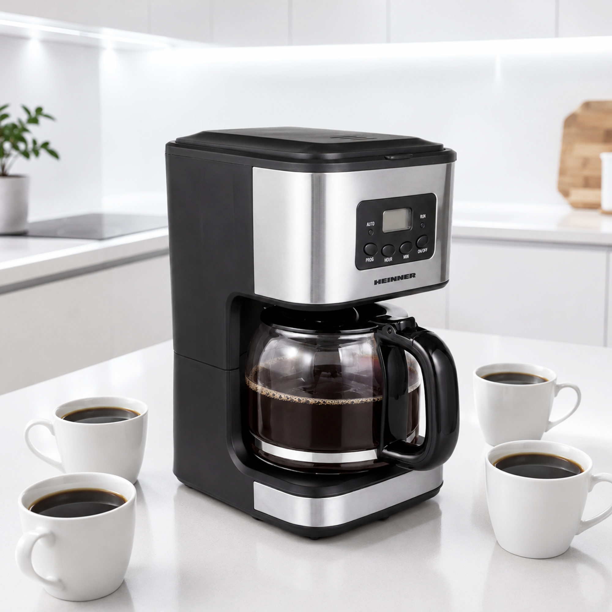A black and silver Heinner coffee maker with glass carafe and four white cups of coffee on a kitchen counter.