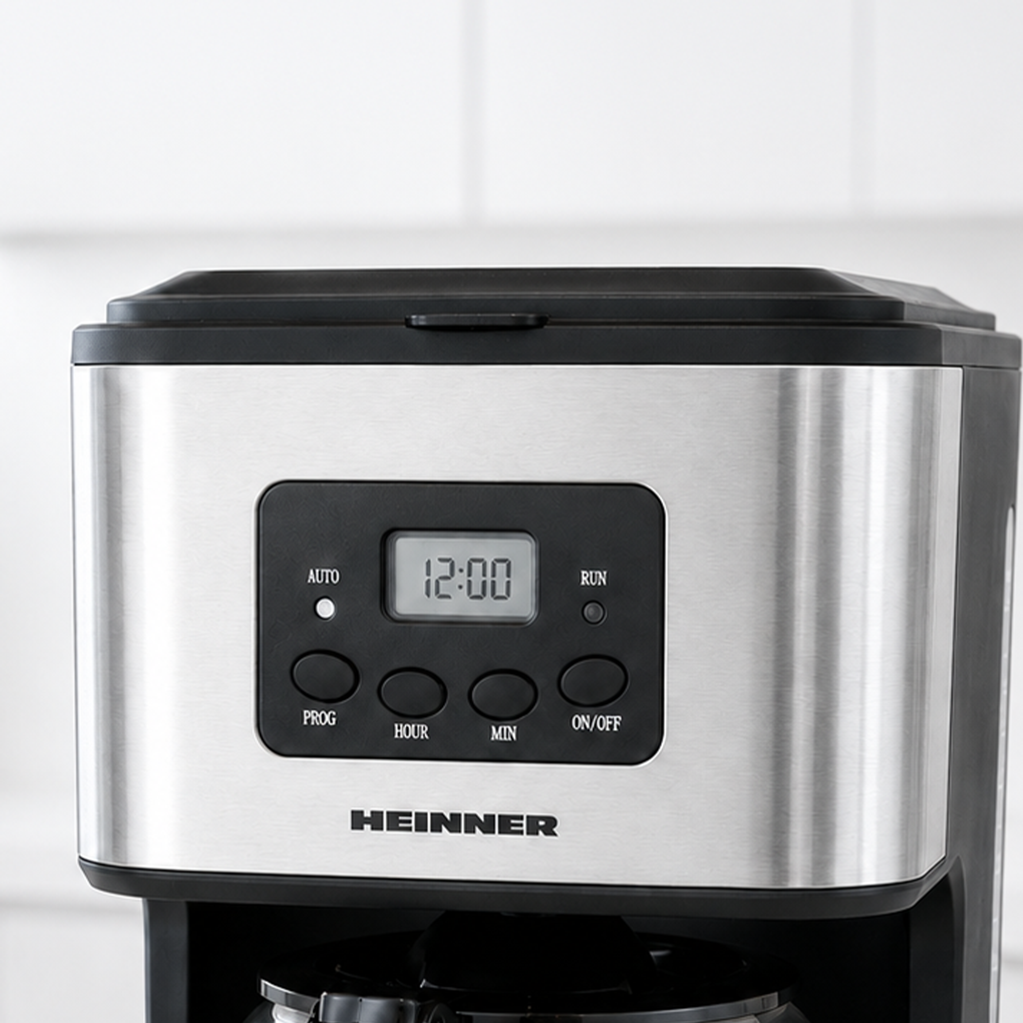 Close-up of a stainless steel Heinner coffee maker with a digital clock display set to 12:00 and control buttons.