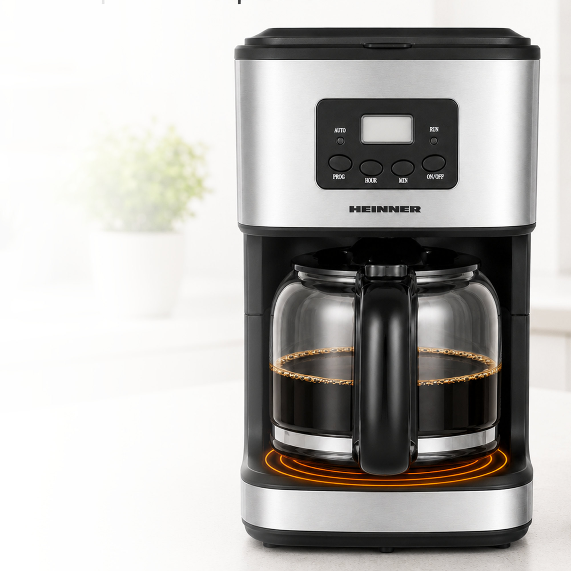 A modern silver and black coffee maker with a glass pot filled with coffee on a warm base.