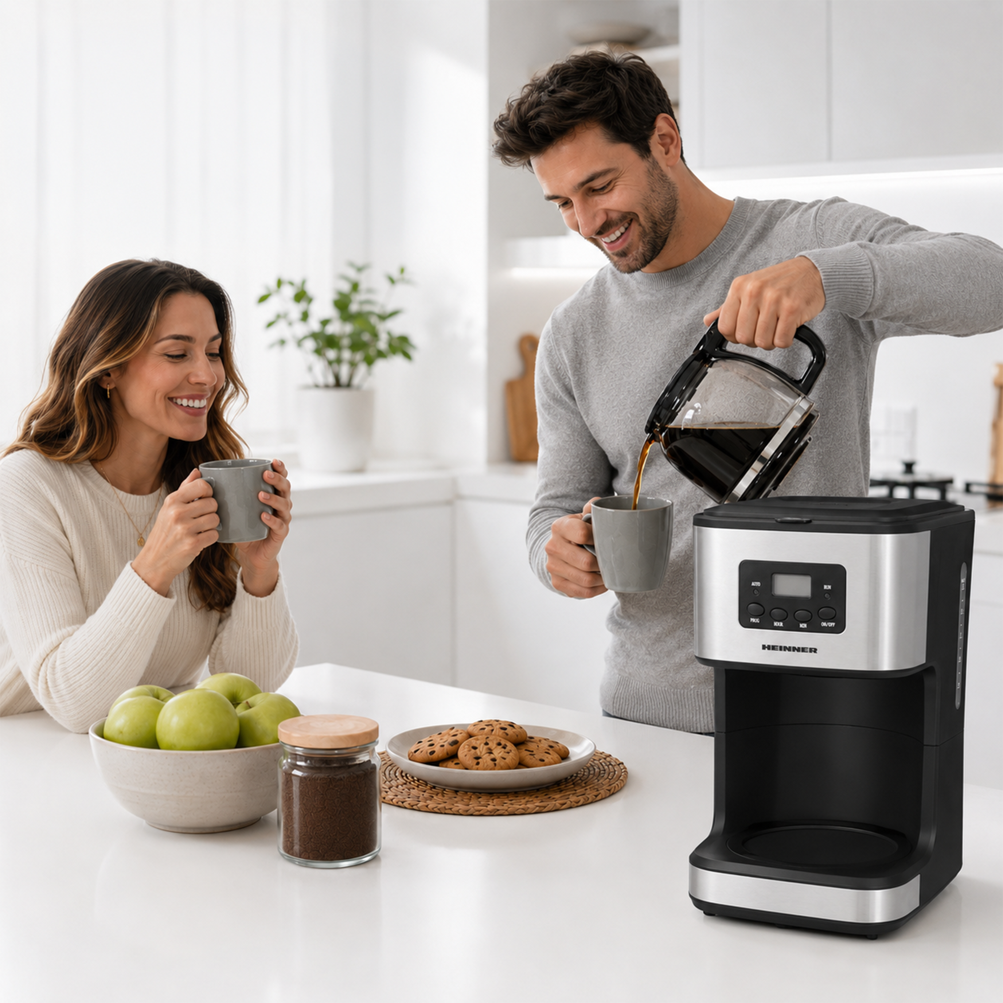 A man pours coffee into a cup while a smiling woman holds one; a bowl of green apples and cookies sit on the kitchen counter.