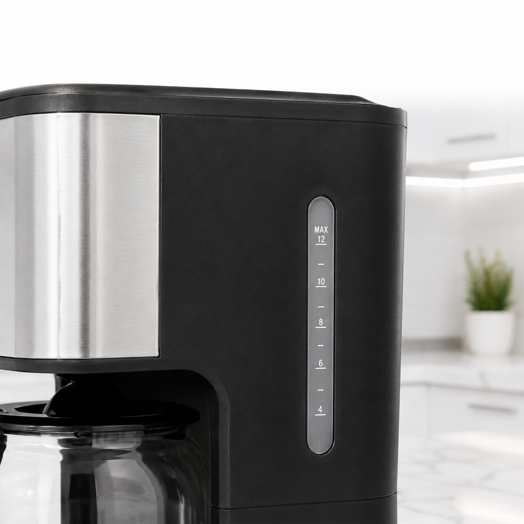 A black and silver coffee maker with a water level indicator in a bright kitchen.
