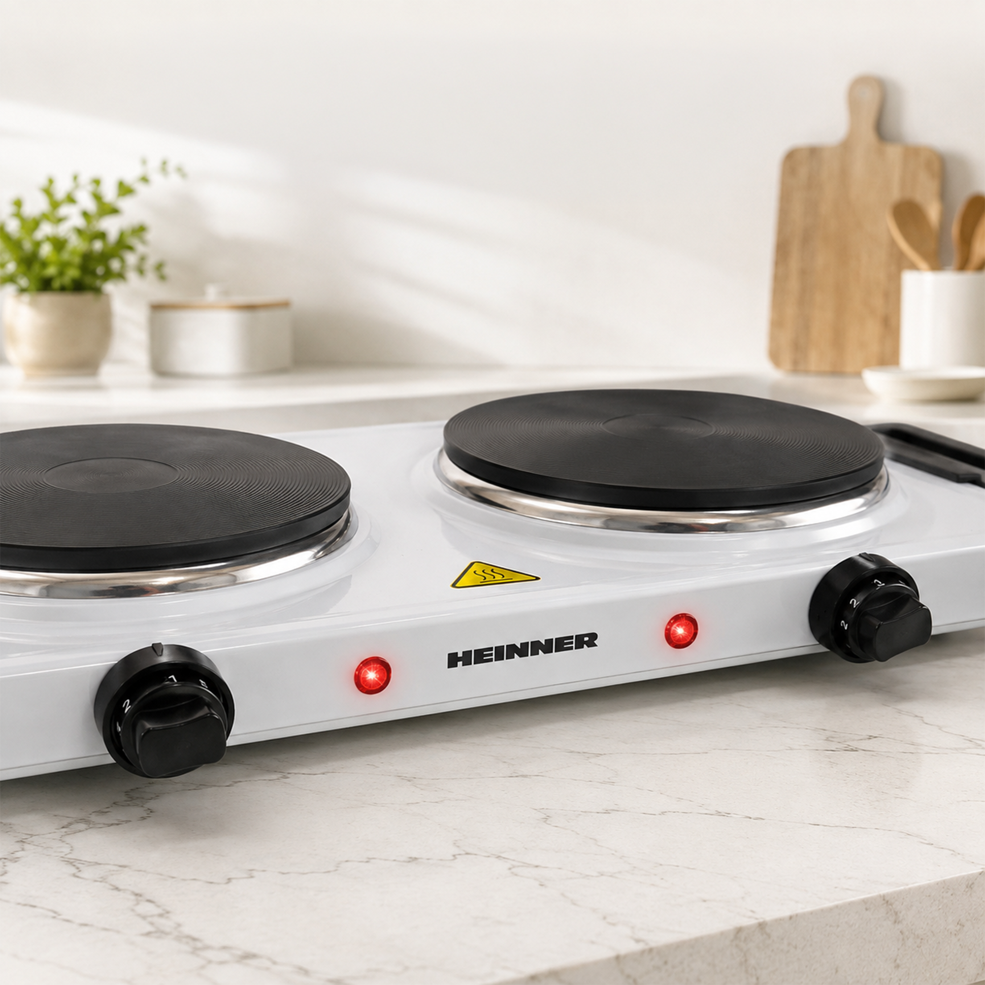 A white double electric hotplate on a marble countertop with two red indicator lights on, in a bright kitchen.