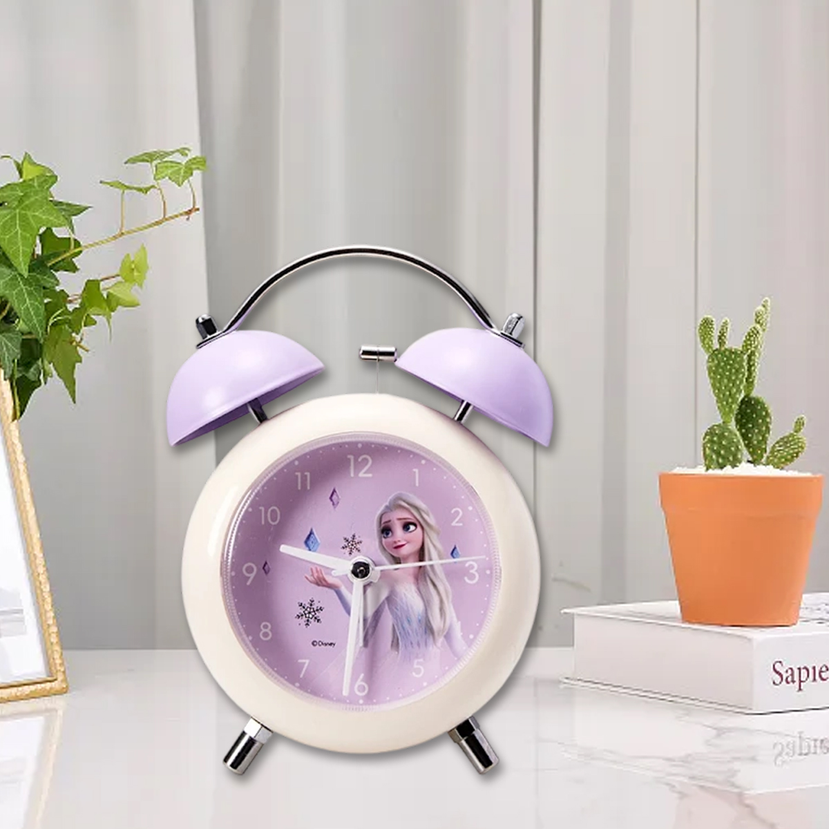 Ein weißer Wecker mit lila Glocken zeigt Elsa aus Frozen auf dem Zifferblatt, flankiert von Pflanzen.