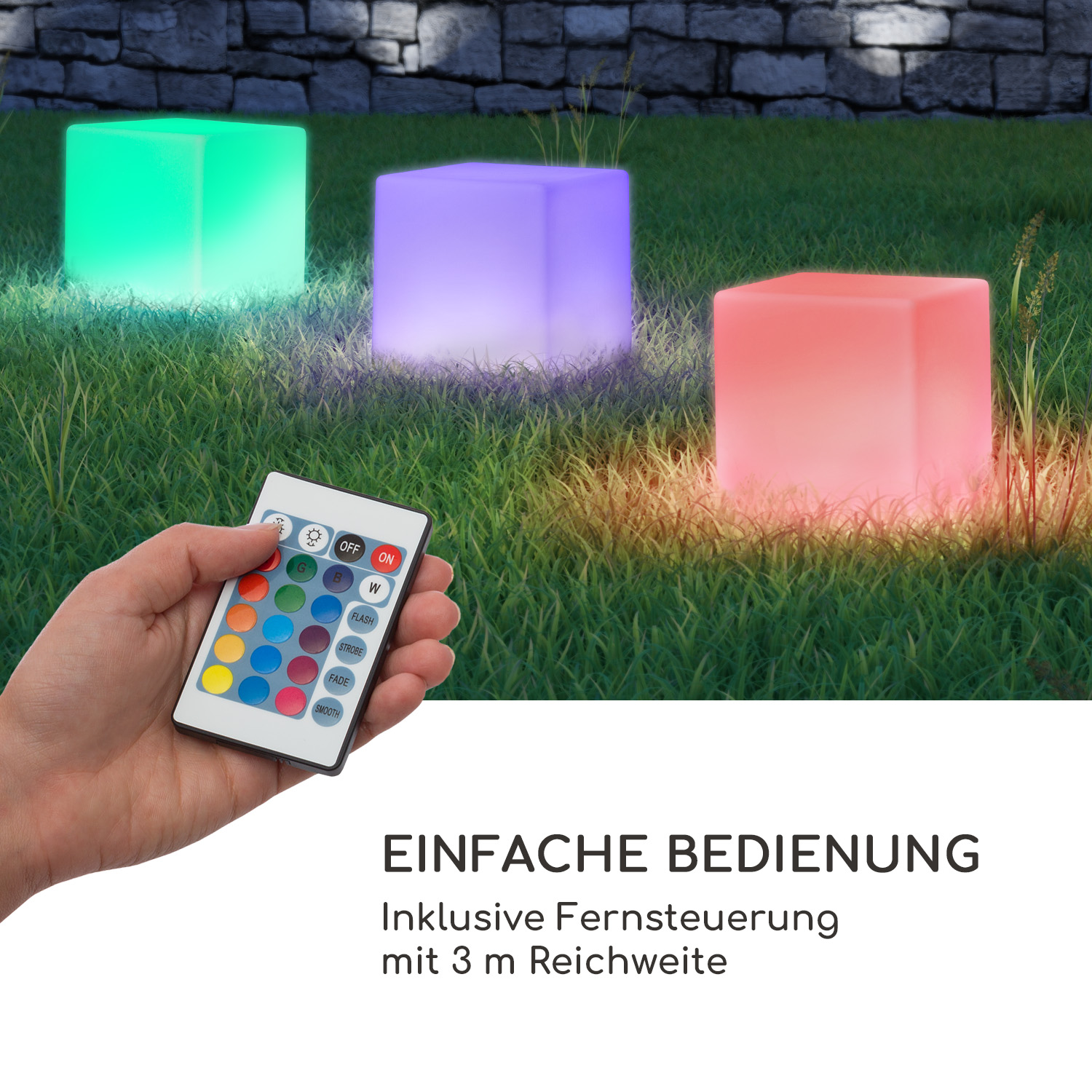 Hand hält Fernbedienung, im Hintergrund drei leuchtende LED-Würfel im Gras vor einer Steinwand.