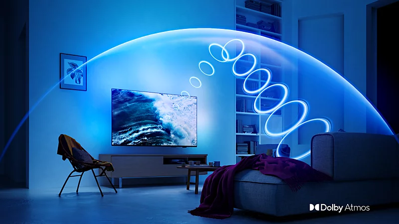 Salon z niebieskim oświetleniem i świecącą kopułą dźwiękową łukiem od telewizora do kanapy, z logo Dolby Atmos.