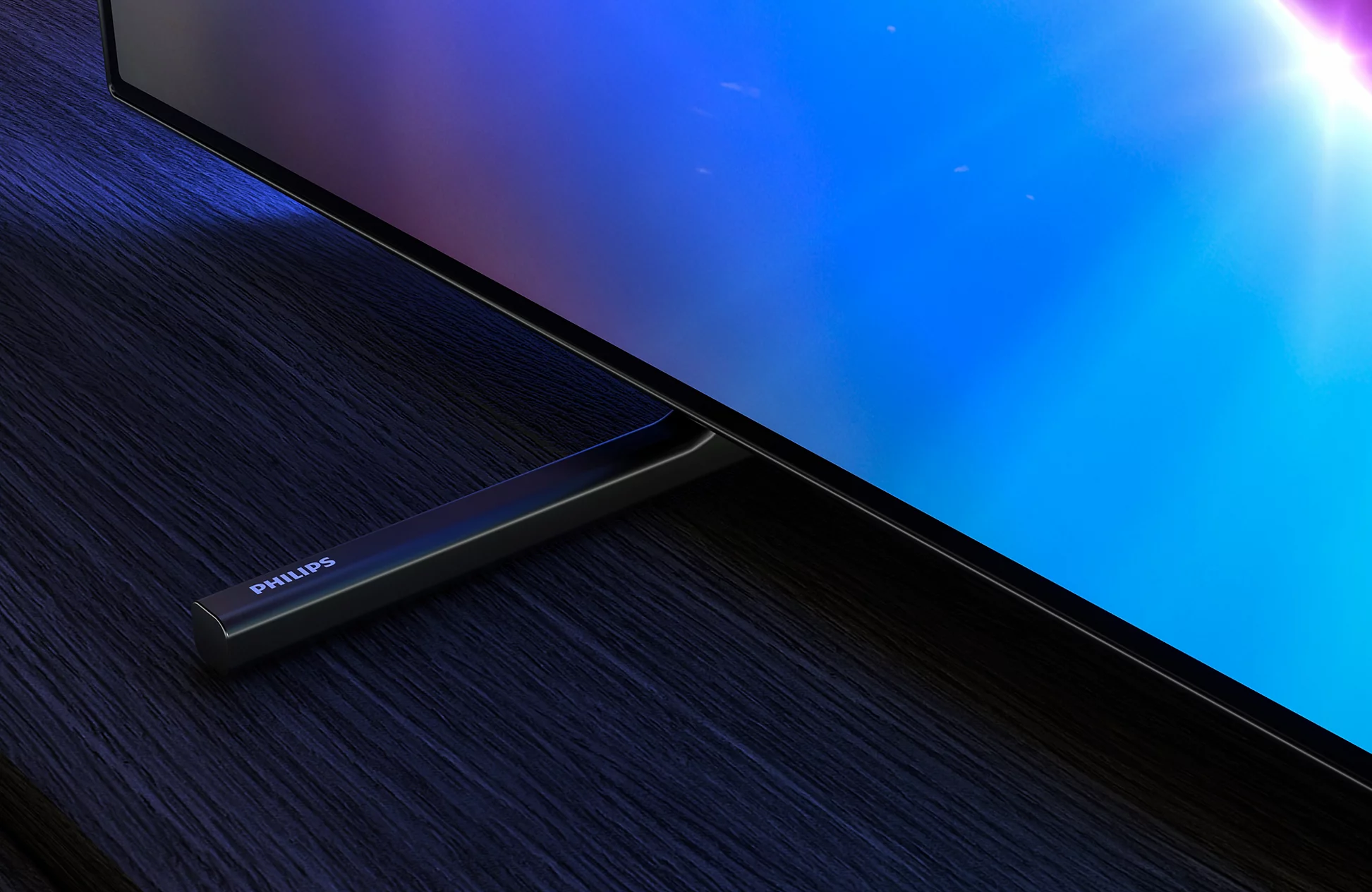Telewizor Philips z czarną podstawą na ciemnym drewnie pokazuje niebieski ekran z jasnym światłem.