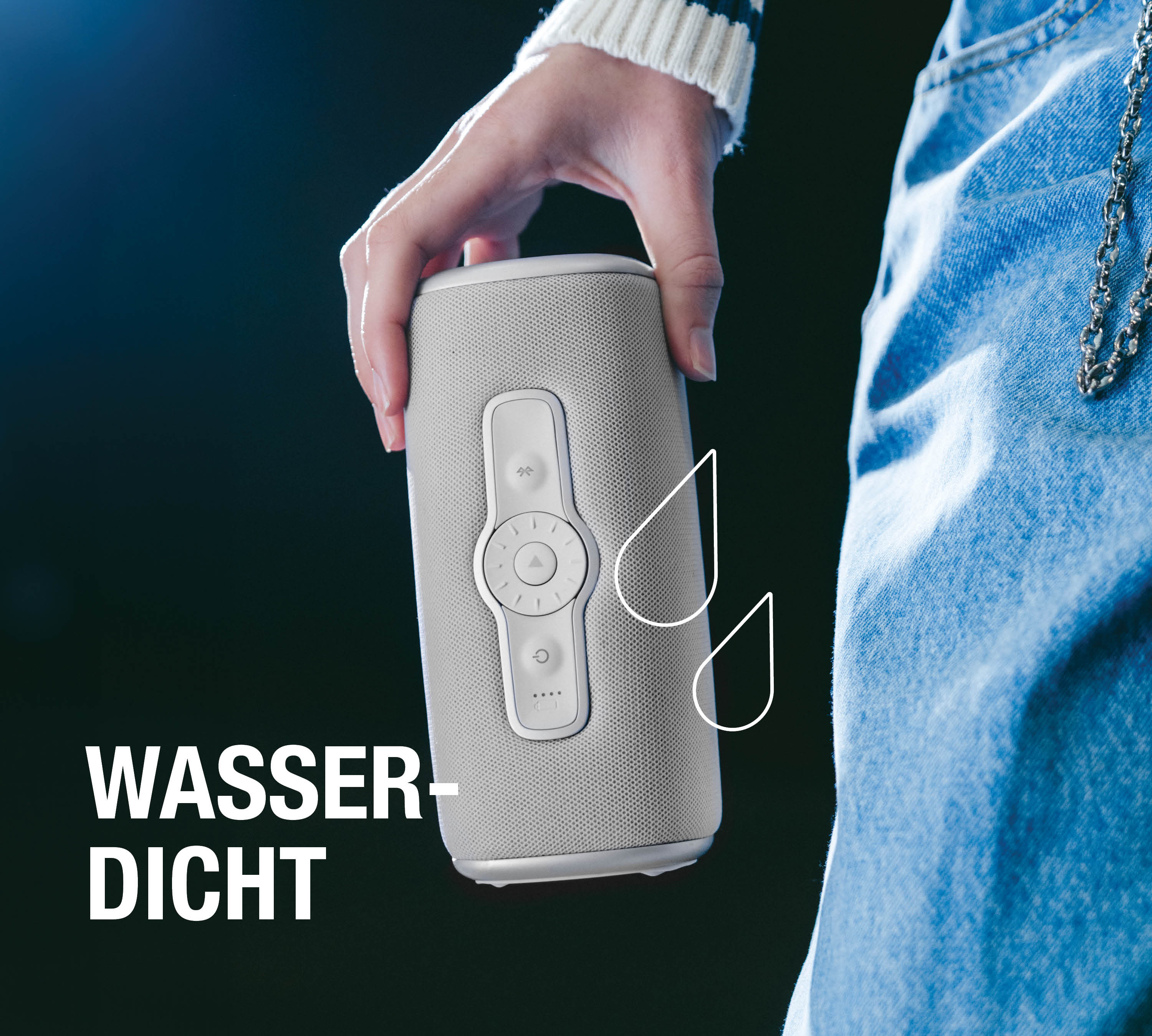 Person in Jeans hält einen grauen, wasserdichten Bluetooth-Lautsprecher.