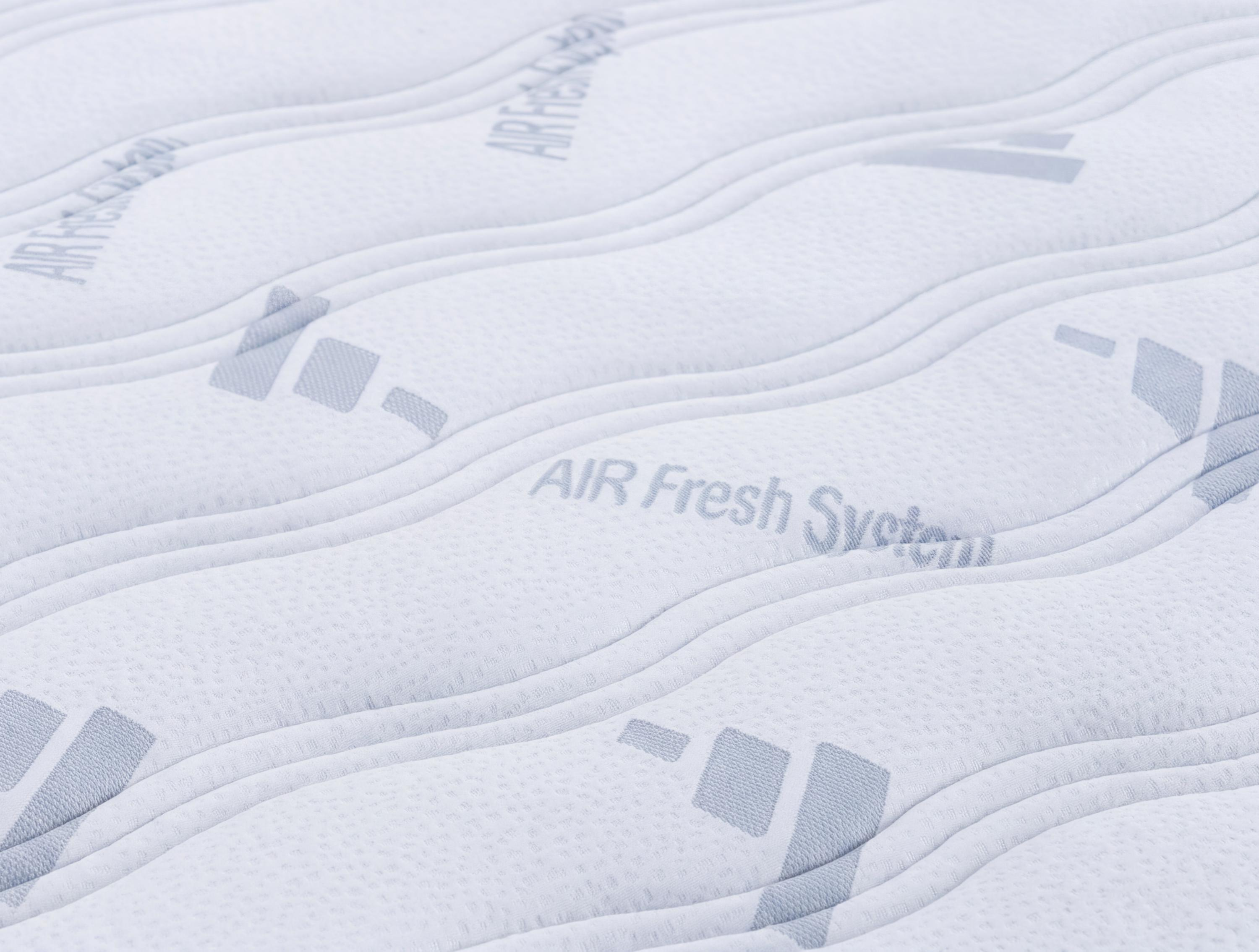 Primer plano de una superficie de colchón blanca acolchada con el texto Air Fresh System y patrones geométricos grises.