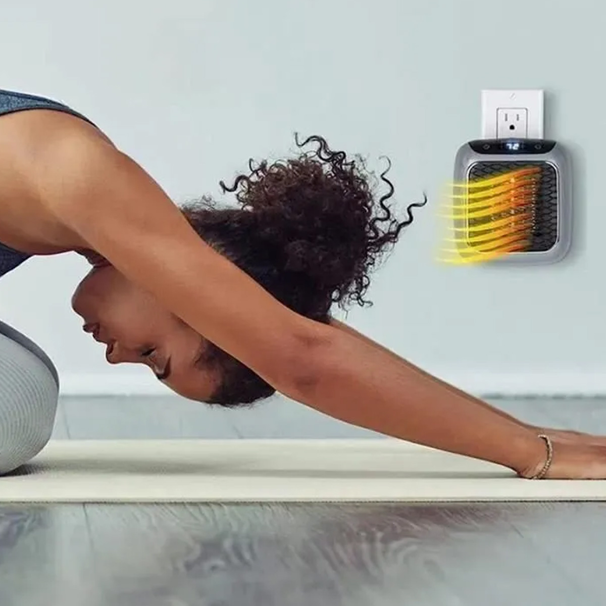 Eine Frau in Yoga-Pose auf einer Matte neben einem kleinen Wandheizer.