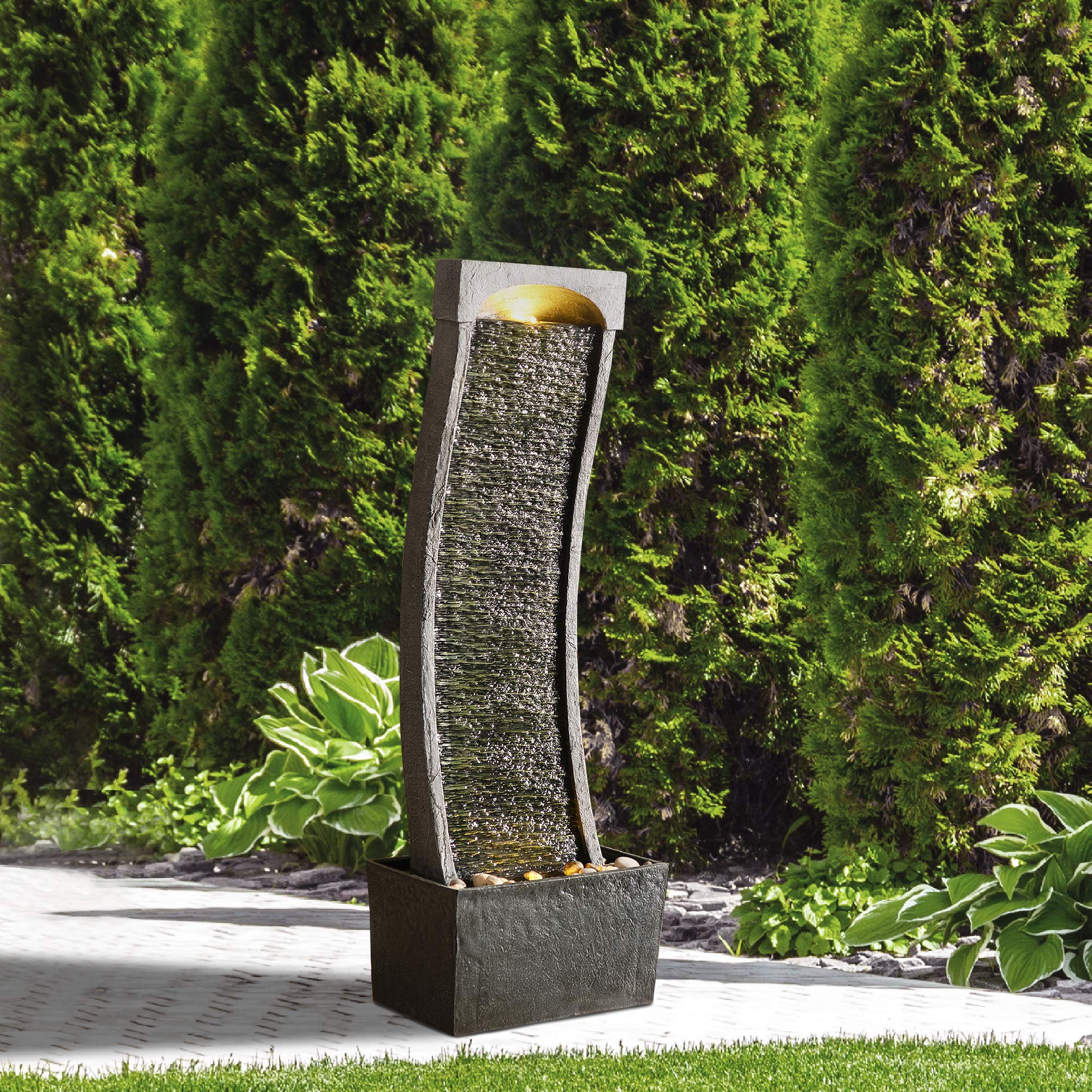 Une fontaine de jardin moderne et incurvée avec un sommet éclairé, devant des arbres verts.