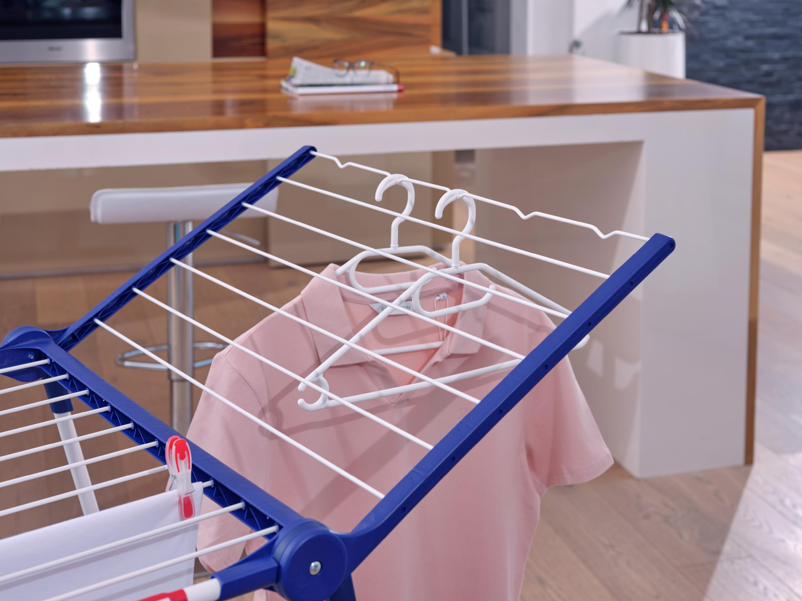 Una polo rosa appesa a una gruccia bianca su uno stendibiancheria blu e bianco in cucina.