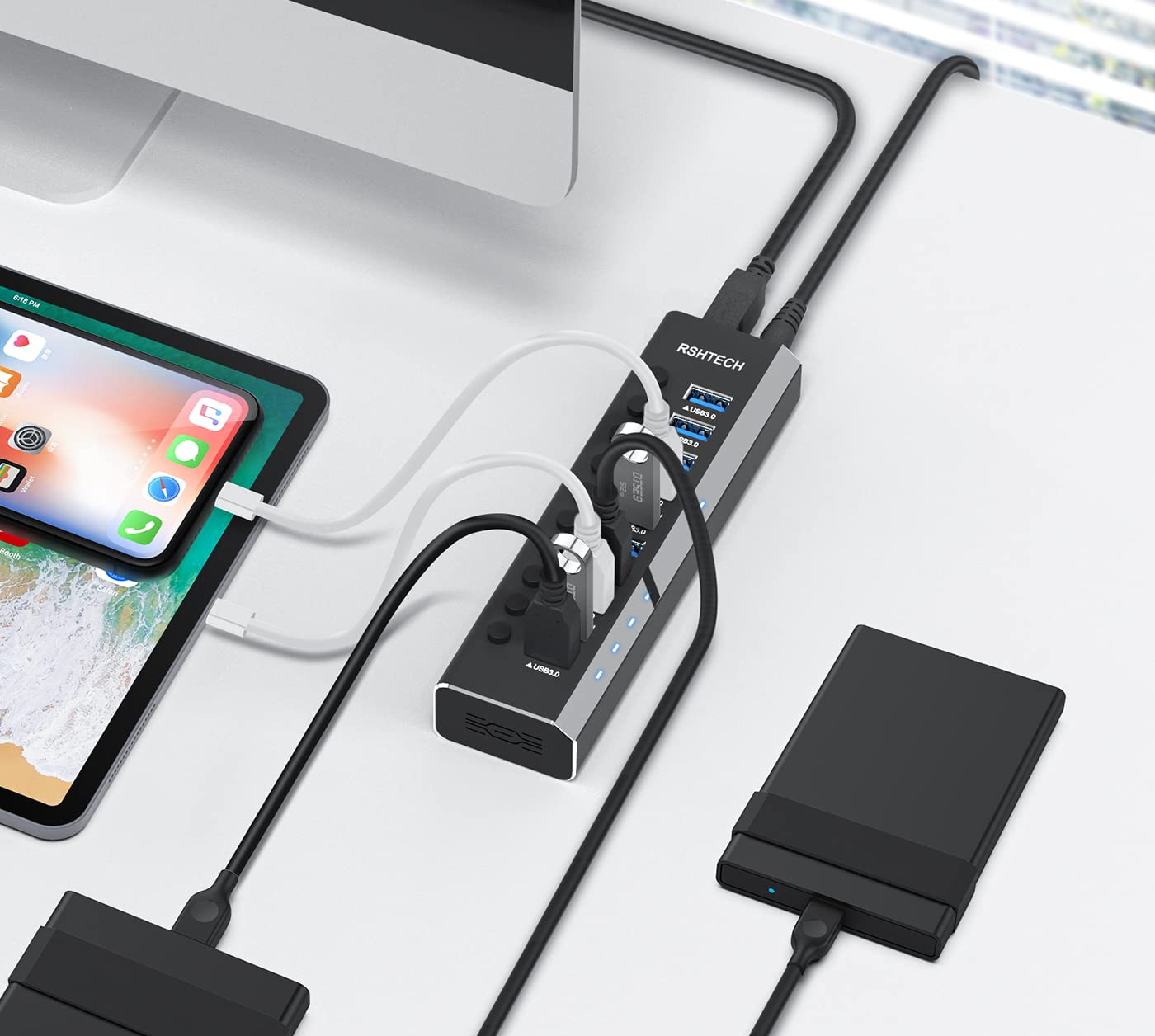 Ein silberner und schwarzer USB-Hub auf einem Schreibtisch mit angeschlossenen Kabeln und Geräten.