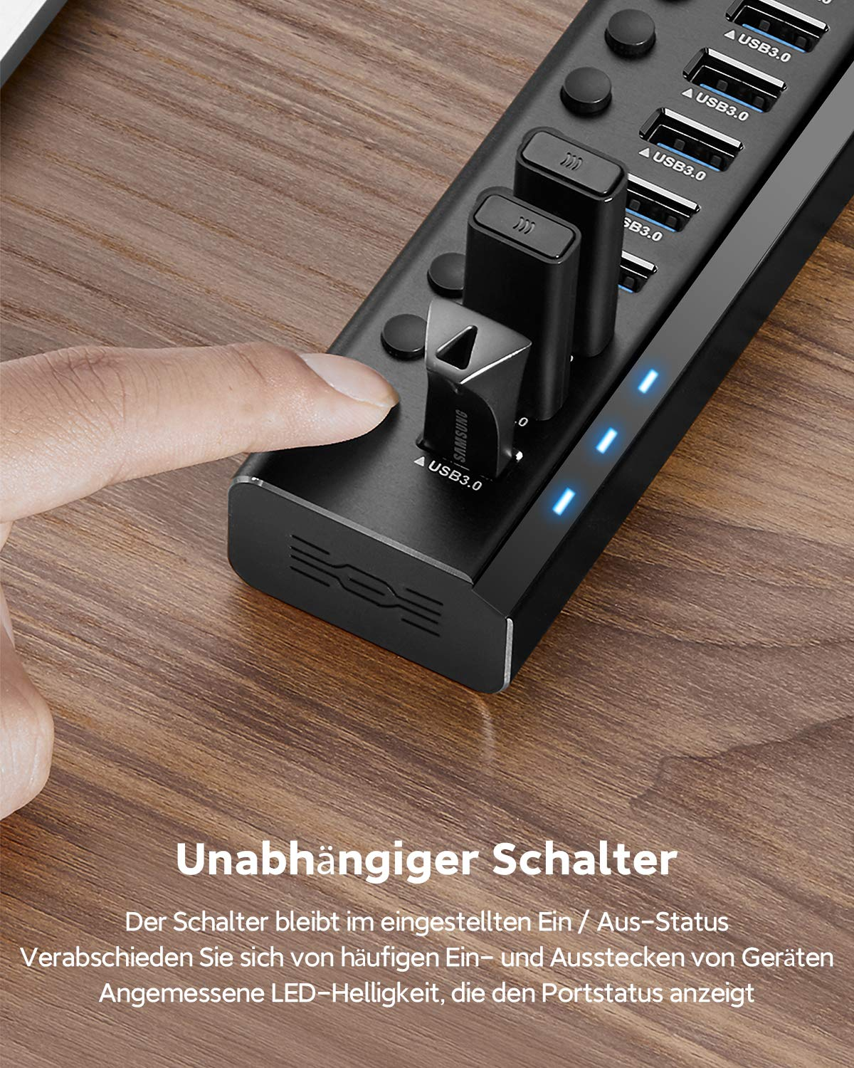 Ein Finger drückt einen Ein-/Ausschalter an einem schwarzen USB-Hub mit eingesteckten USB-Sticks auf einem Holztisch.