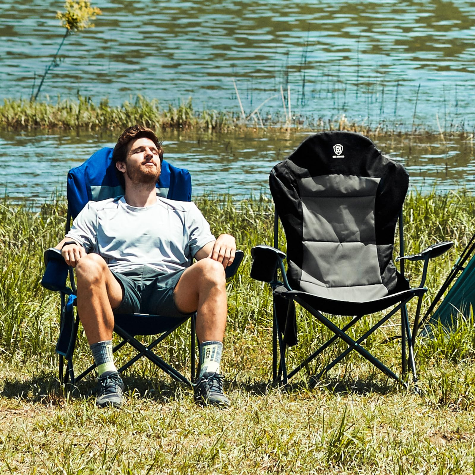 Un uomo si rilassa su una sedia da campeggio vicino a un lago, con un'altra sedia vuota accanto.