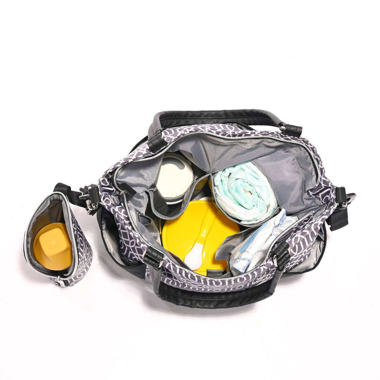 Eine geöffnete Wickeltasche mit Muster zeigt gelbe Dosen, Windeln und Zubehör auf weißem Hintergrund.