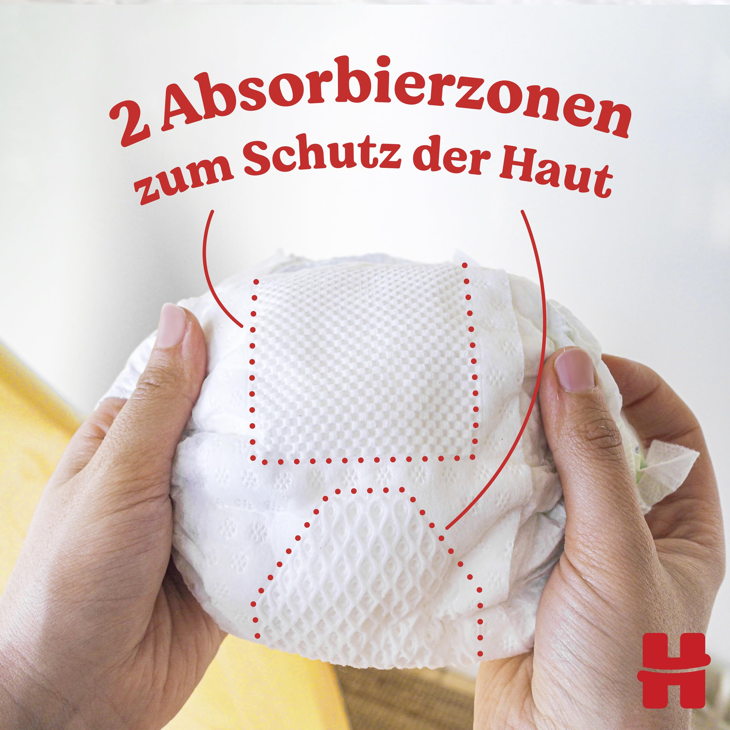 Hände halten eine Windel mit zwei roten Linien markierten Absorbierzonen und der Aufschrift über Schutz der Haut.