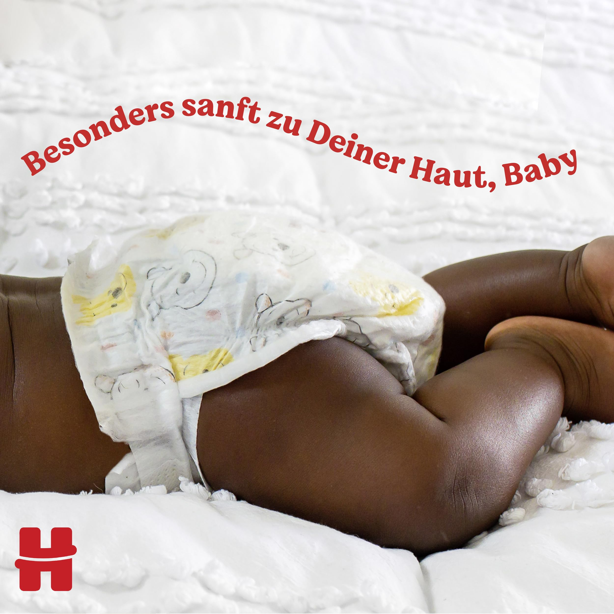 Ein Baby in einer gemusterten Windel liegt auf einer weissen Decke mit rotem Text oben.