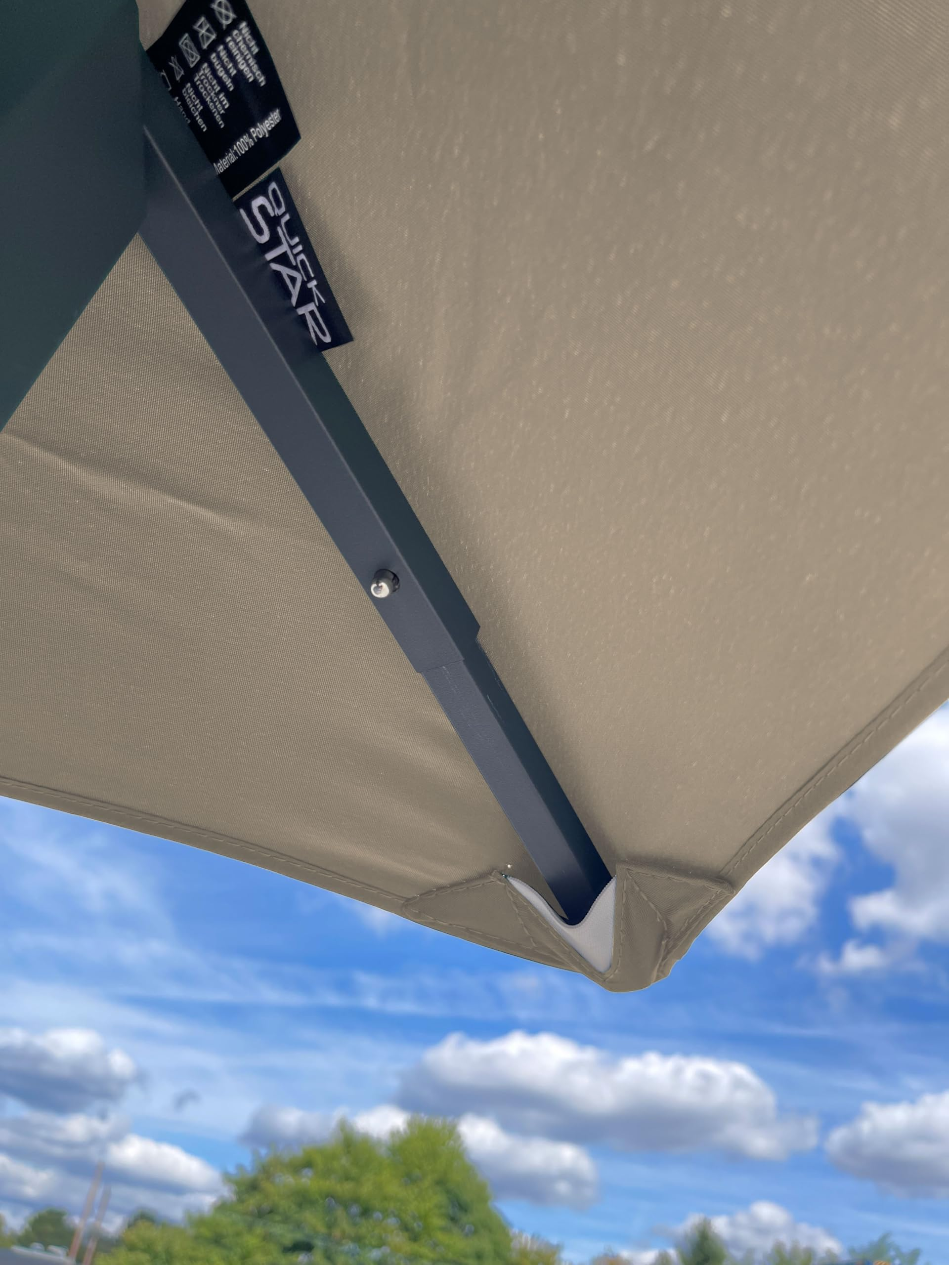 Unterseite eines beige Sonnenschirms mit Metallstrebe vor blauem Himmel mit Wolken.