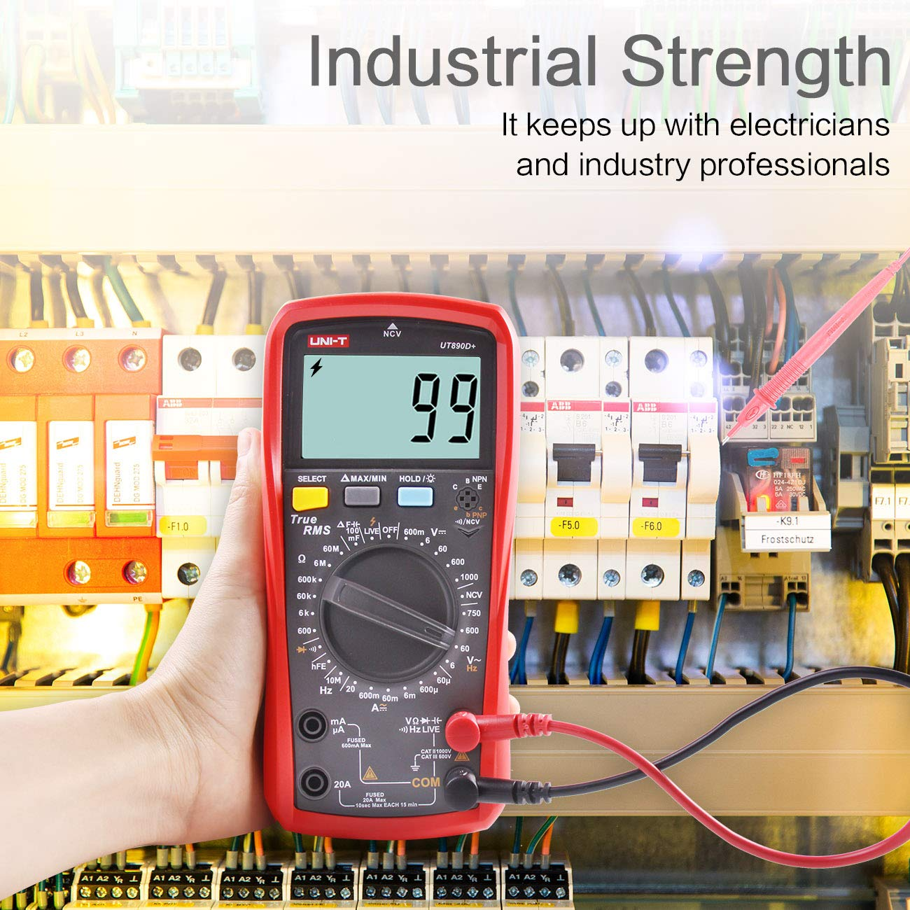 Eine Hand hält ein rotes Digitalmultimeter vor einen Stromkasten mit verkabelten Komponenten.