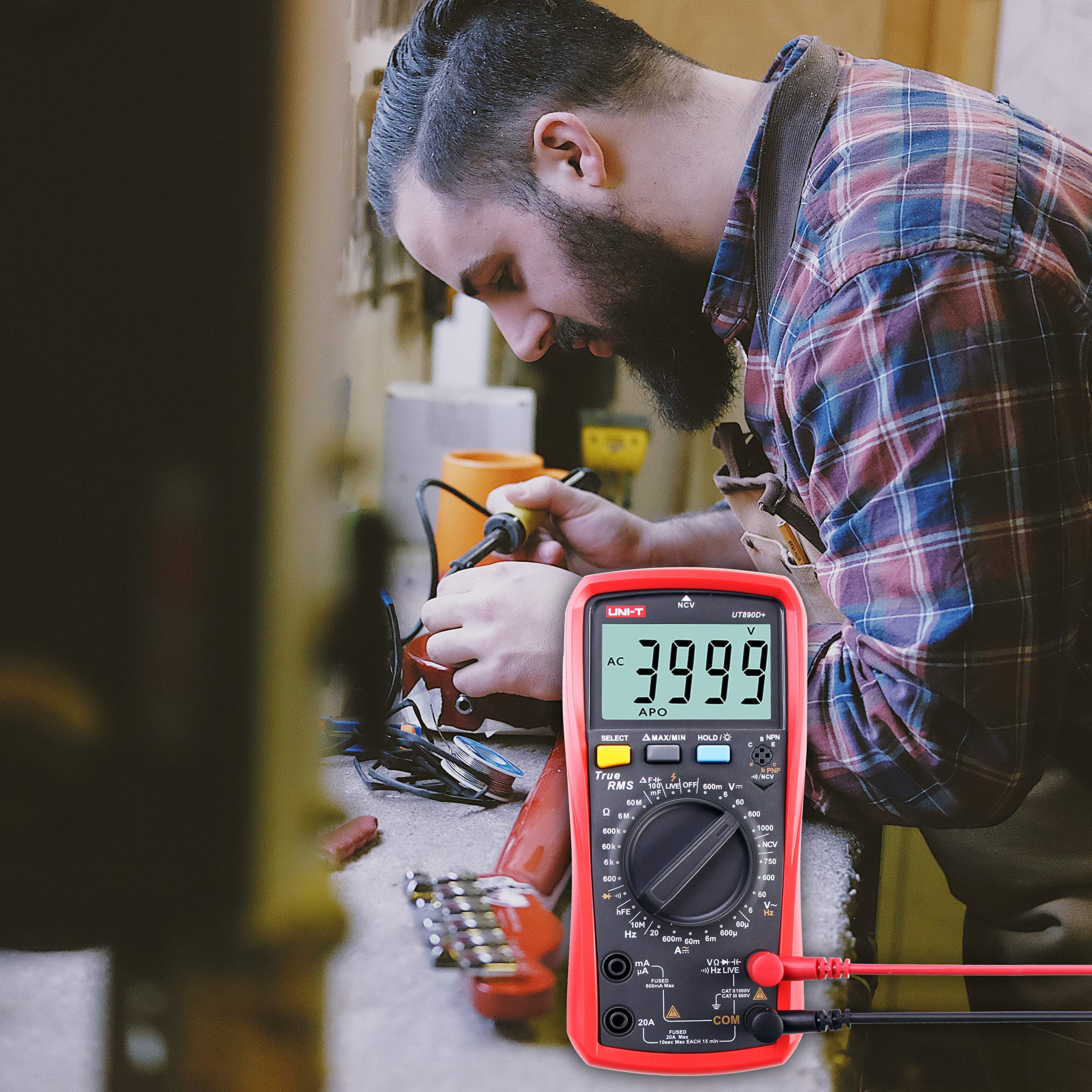 Ein Techniker lötet eine Gitarre in einer Werkstatt, im Vordergrund ein rotes Digitalmultimeter.