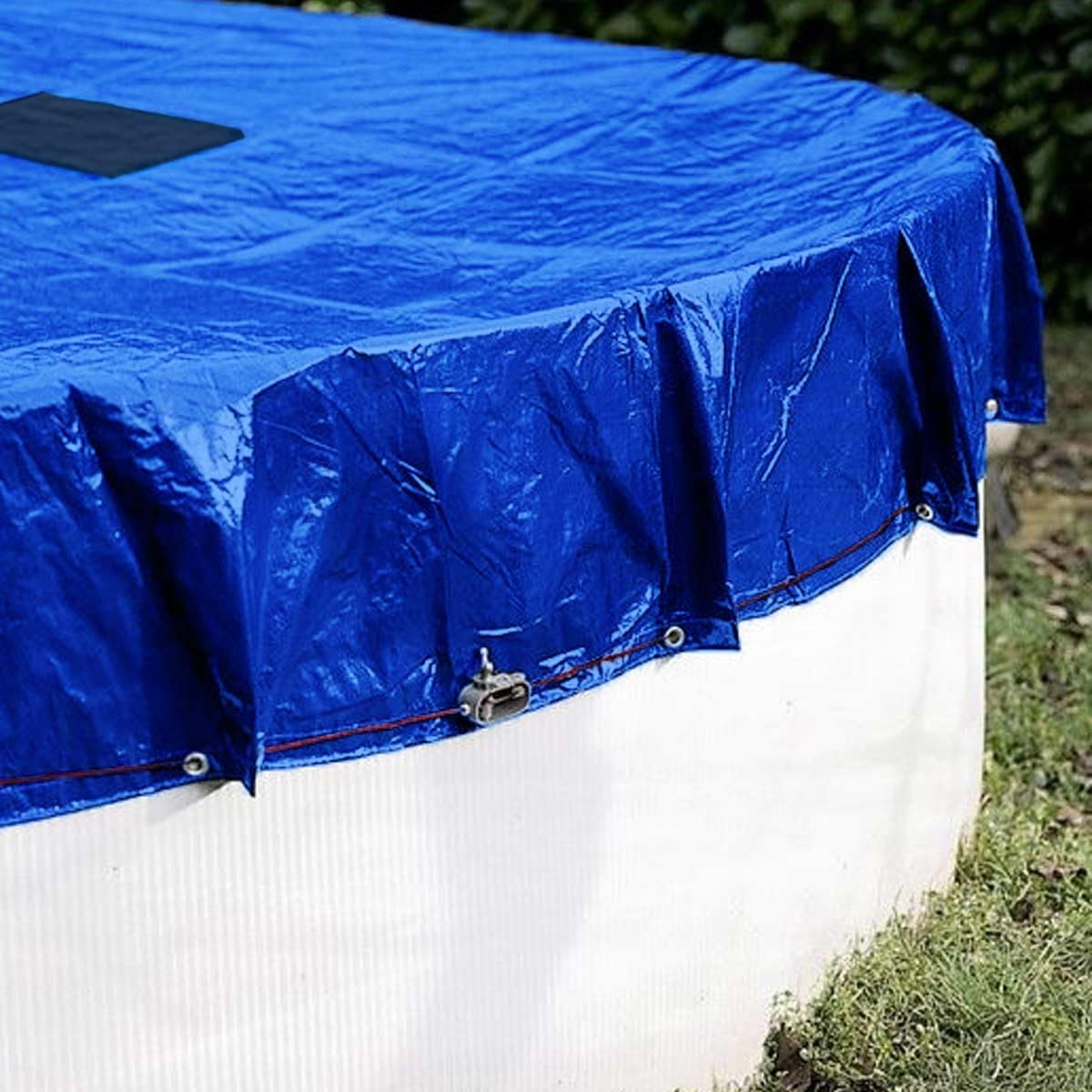 Une bâche de piscine bleue est fixée fermement sur une piscine ronde blanche avec un cordon et une pince.