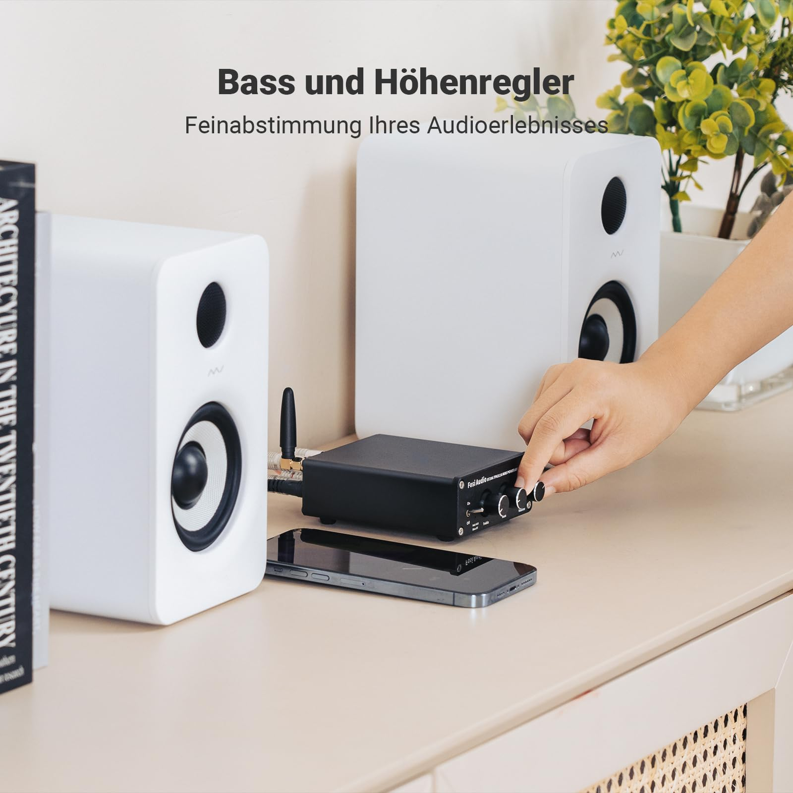 Eine Hand stellt die Regler an einem schwarzen Audioverstärker ein, flankiert von zwei weißen Lautsprechern.