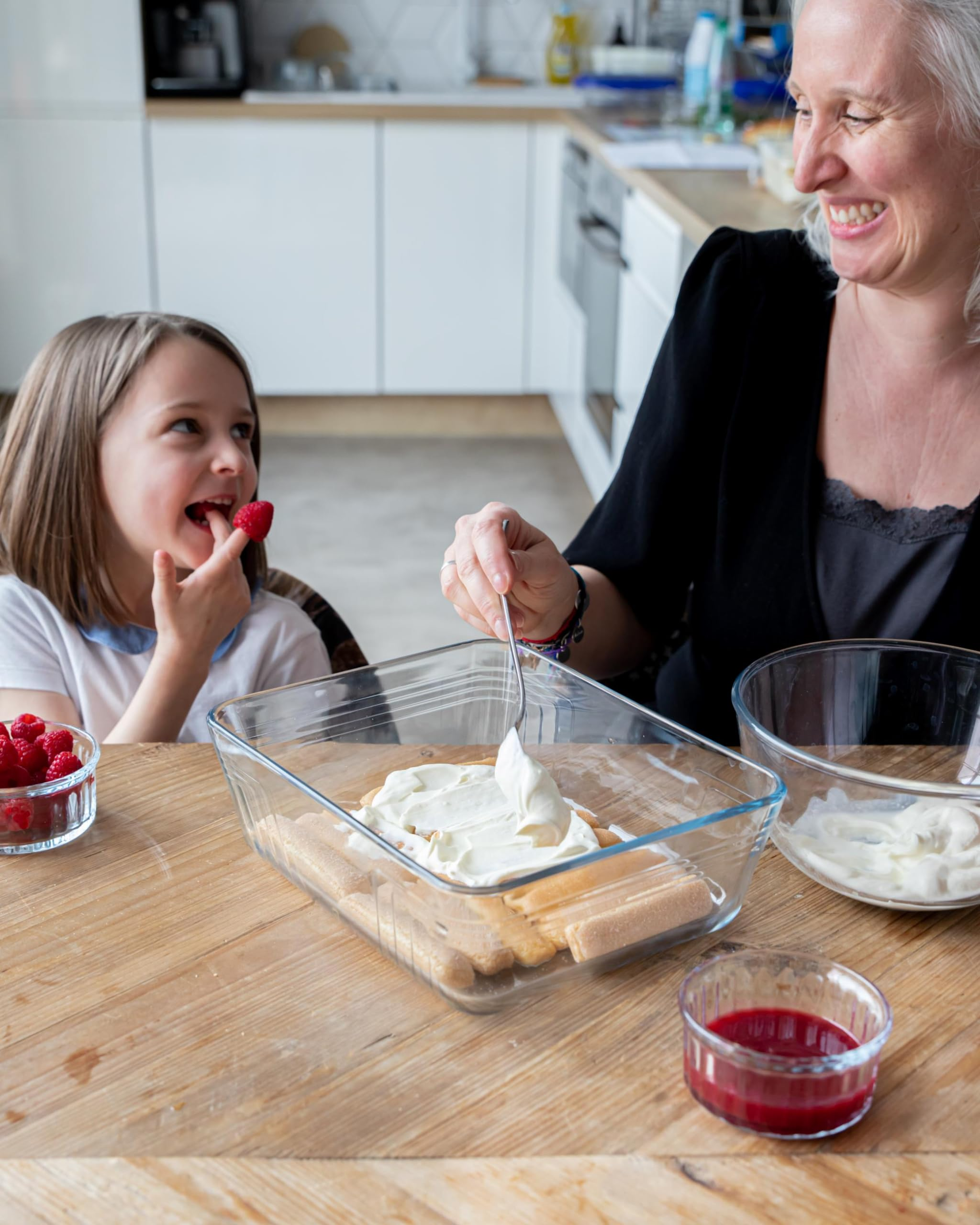 Mutter und Kind bereiten in der Küche ein Dessert zu, während das Kind nascht.