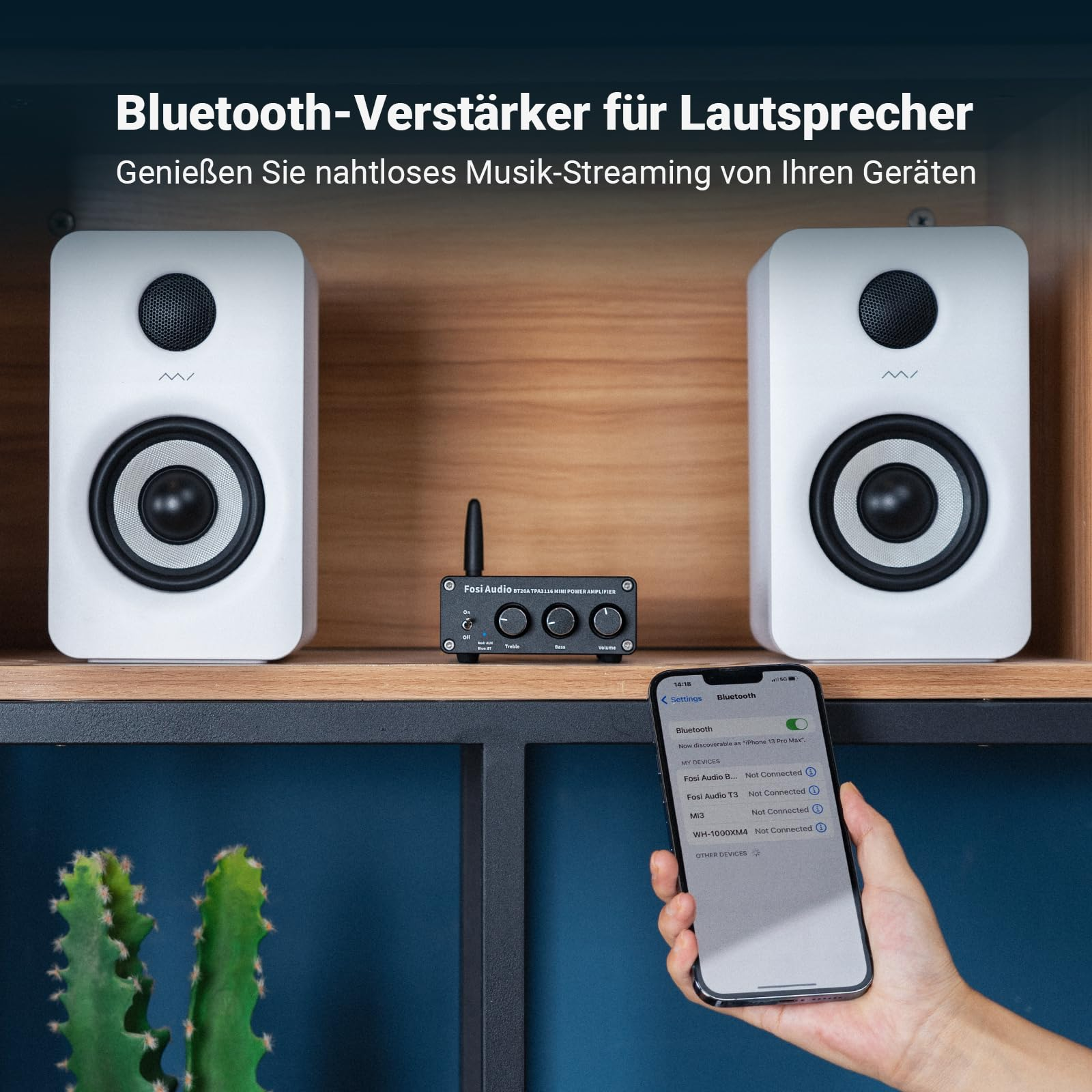 Zwei weiße Lautsprecher, ein schwarzer Mini-Verstärker und eine Hand mit Smartphone vor einem hölzernen Regal.