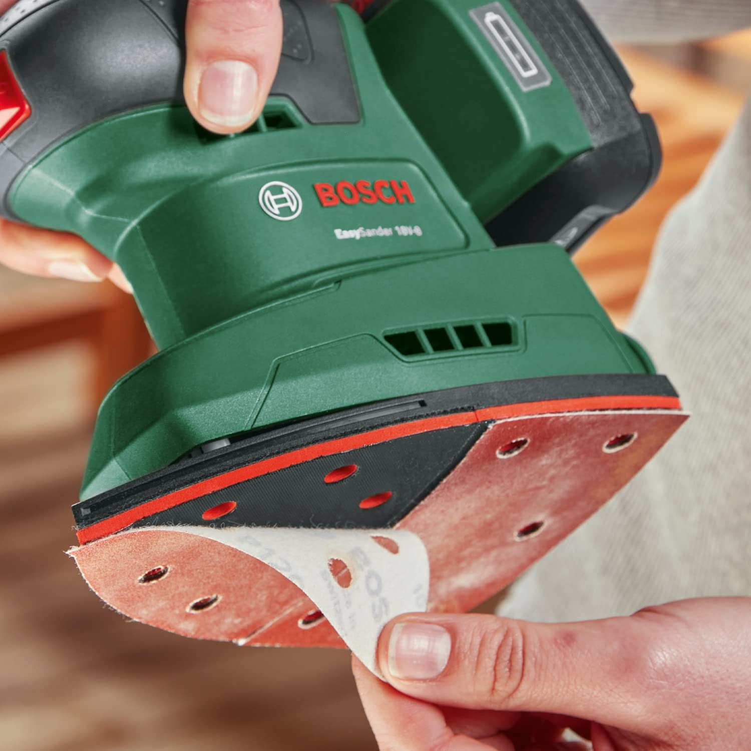 Person wechselt das Schleifpapier an einer grünen Bosch Akku-Multischleifer.