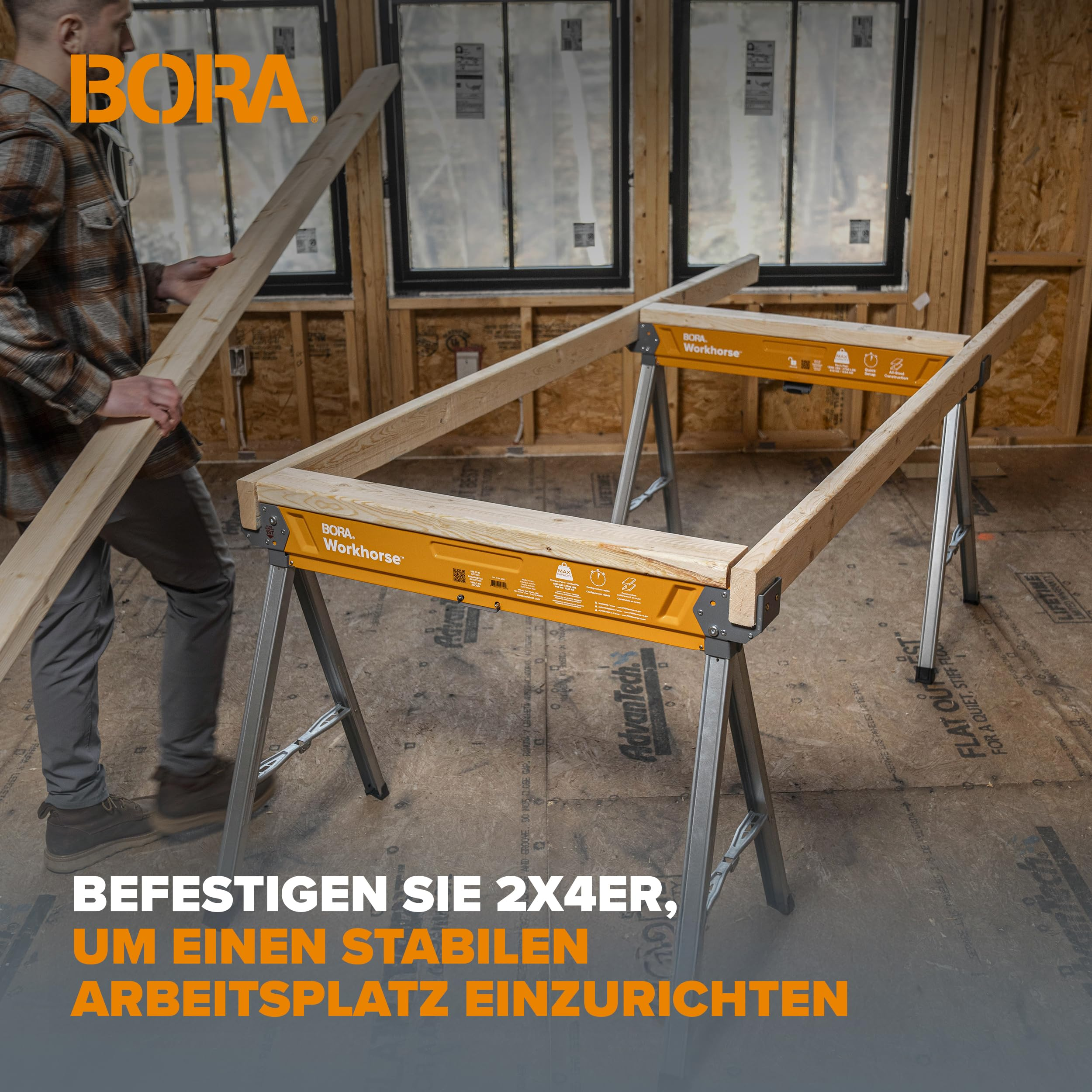 Ein Mann trägt Holz zu zwei orangen und grauen Bora Workhorses, die als Werkbank in einem Rohbau stehen.