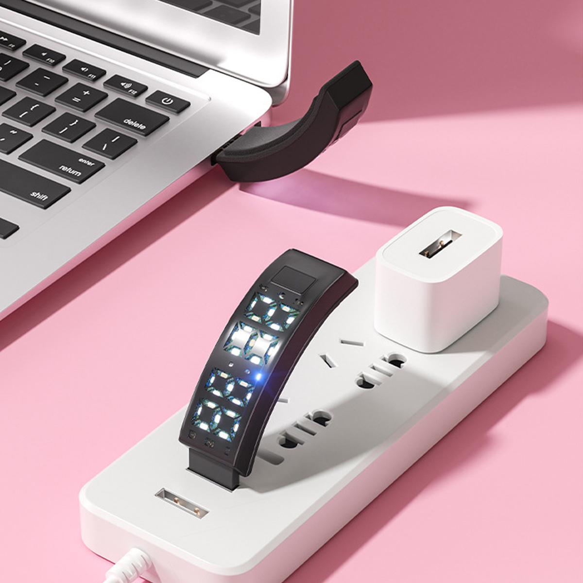 Ein Laptop, eine Powerbank und eine Steckdosenleiste auf einer rosafarbenen Oberfläche.