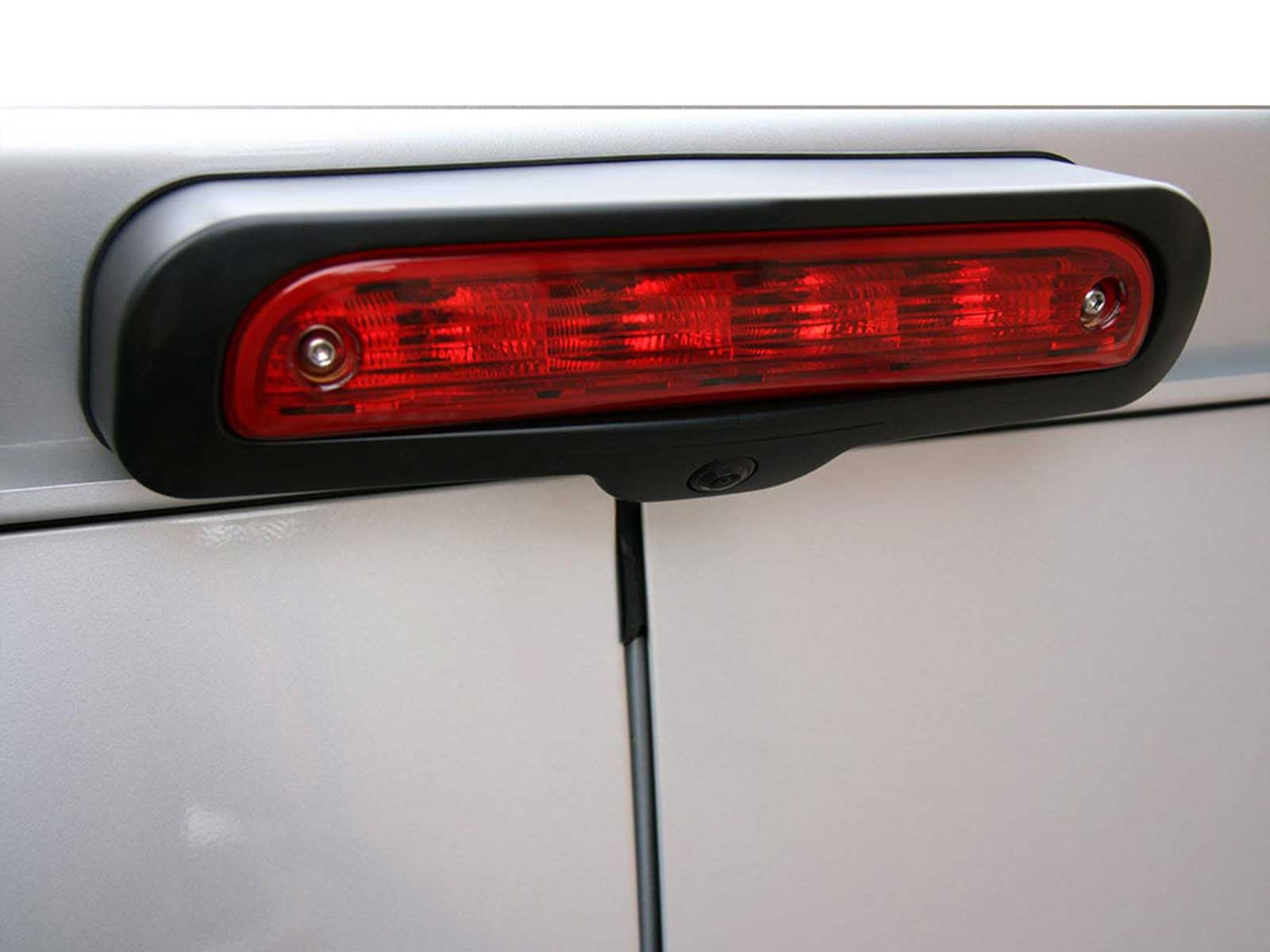 Rotes Auto-Bremslicht mit schwarzem Rahmen an einer silbernen Karosserie.