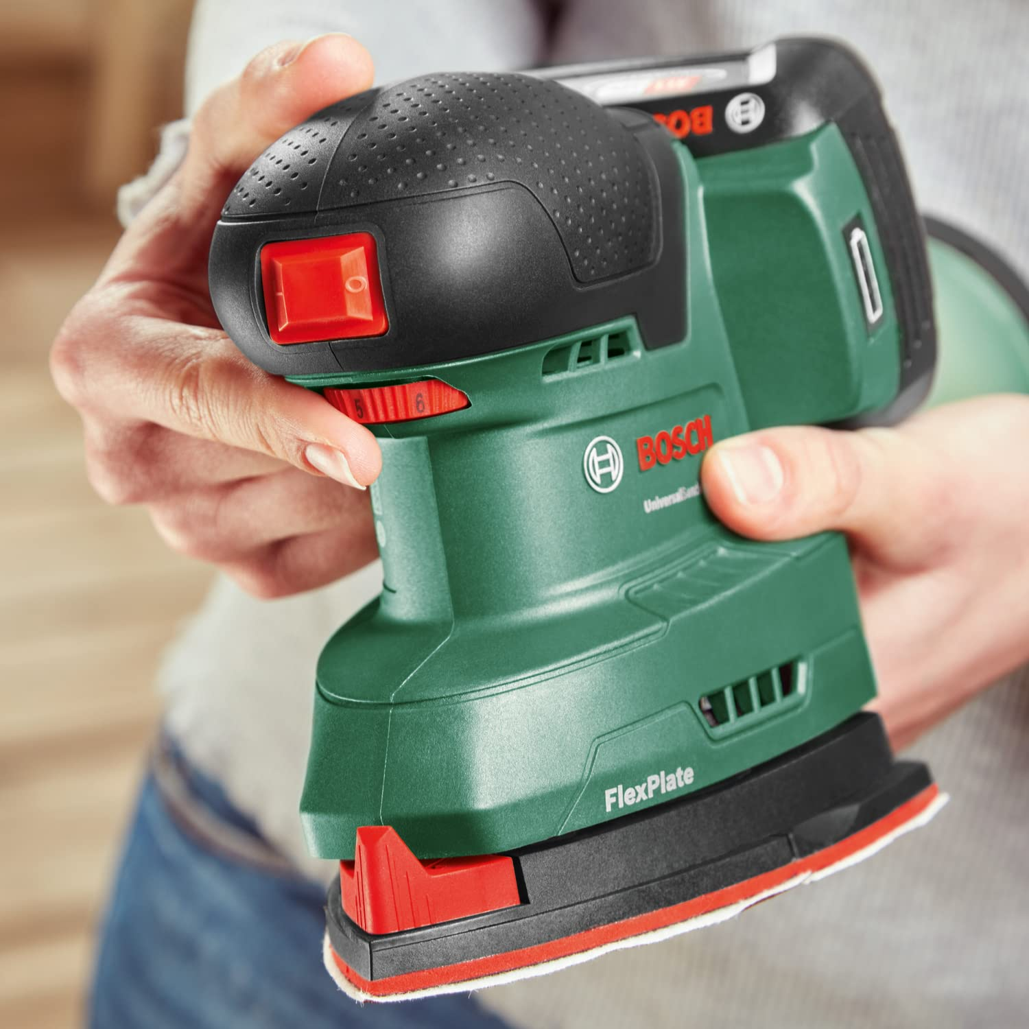 Eine Person hält einen grünen und schwarzen Bosch Akku-Multischleifer.