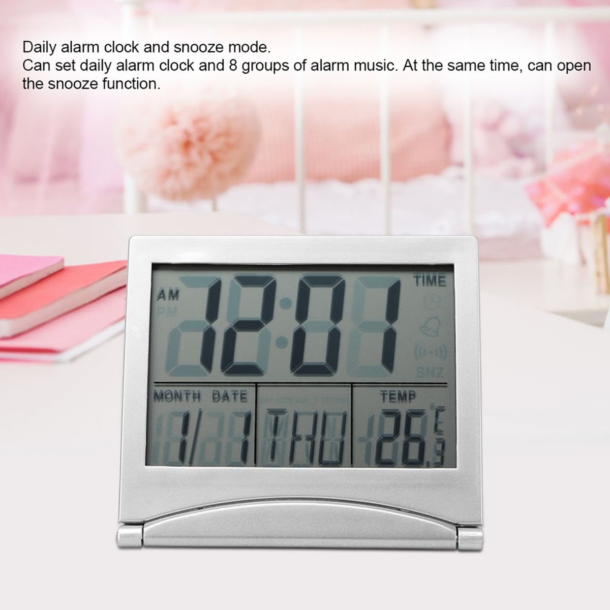 Silberner Digitalwecker mit grossem Display zeigt Uhrzeit, Datum, Wochentag und Temperatur. Im Hintergrund rosafarbener Raum.