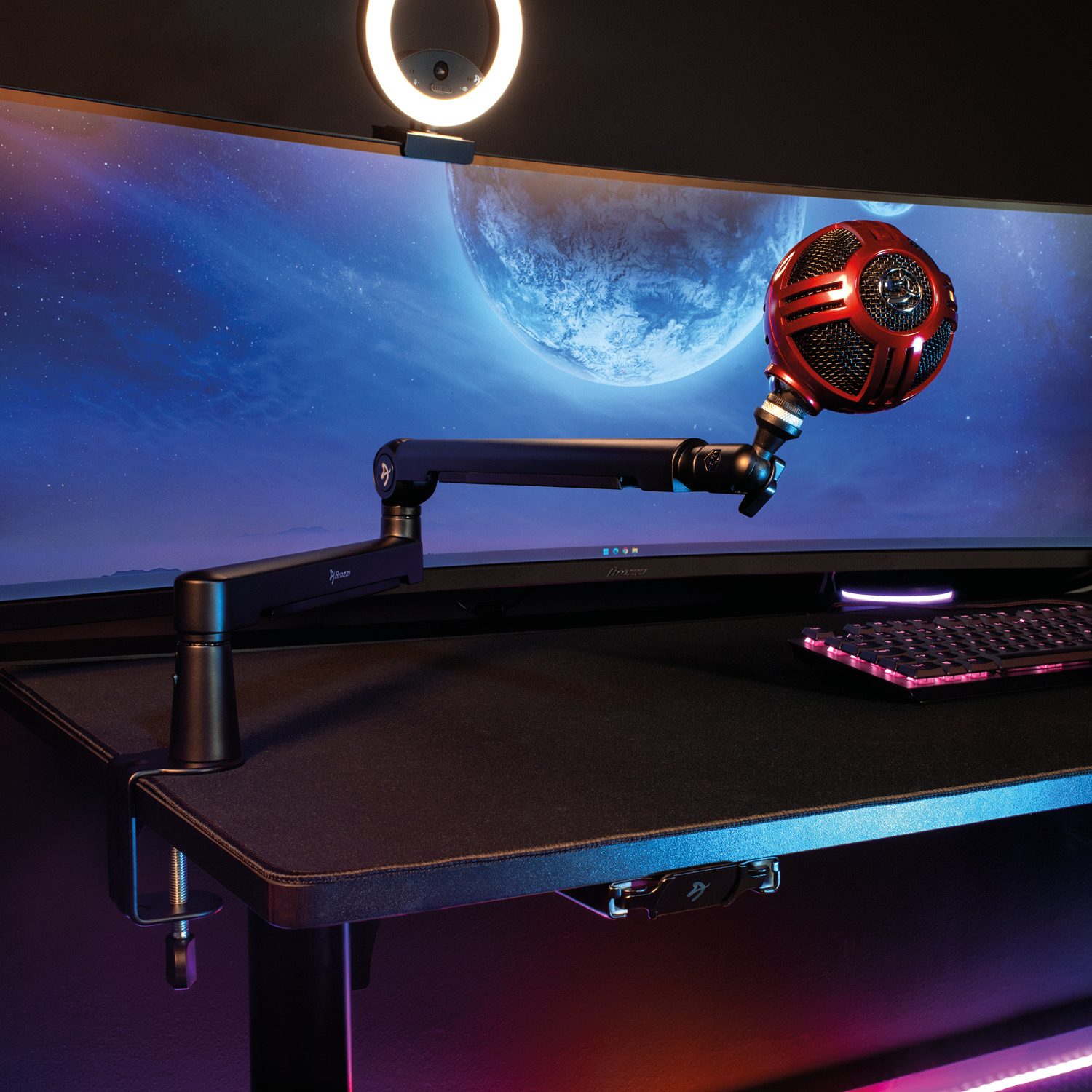 Ein rotes Mikrofon an einem Schwenkarm auf einem Schreibtisch mit gebogenem Monitor und leuchtendem Ringlicht.