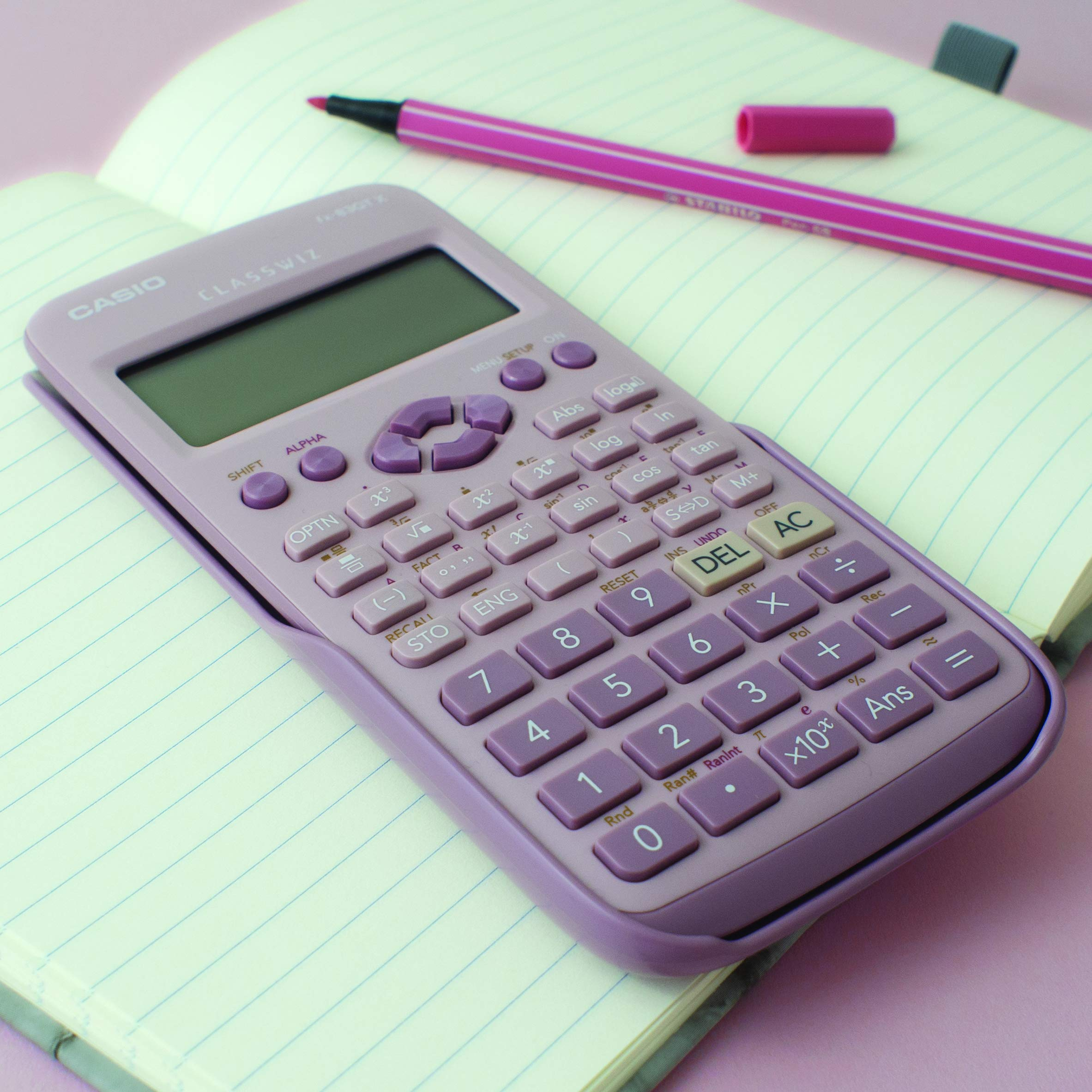 Una calcolatrice viola Casio ClassWiz e una penna rosa poggiano su un quaderno a righe aperto.