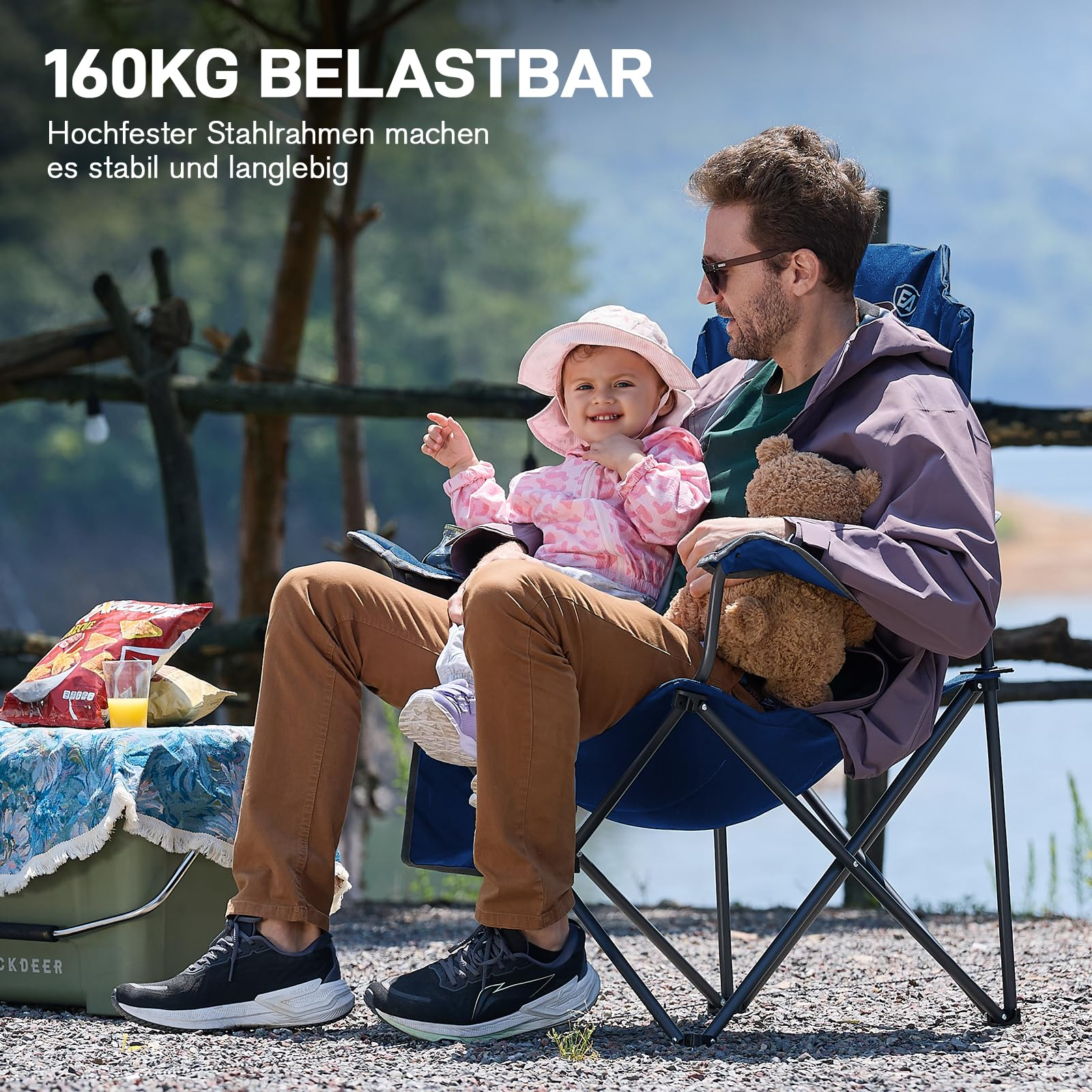 Un padre siede con la sua bambina in una sedia da campeggio blu all'aperto, con la natura sullo sfondo.