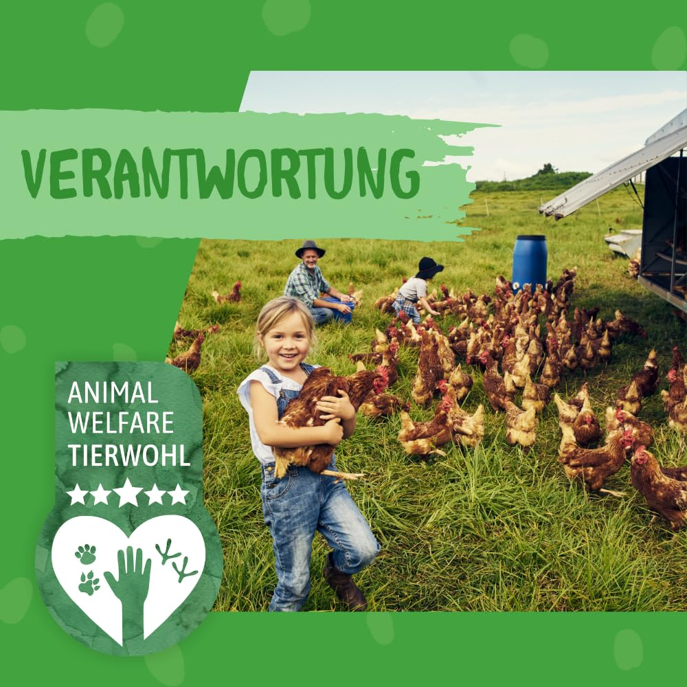 Ein smiling Mädchen hält Hühner auf einer grünen Wiese, im Hintergrund arbeiten Menschen mit Tieren.