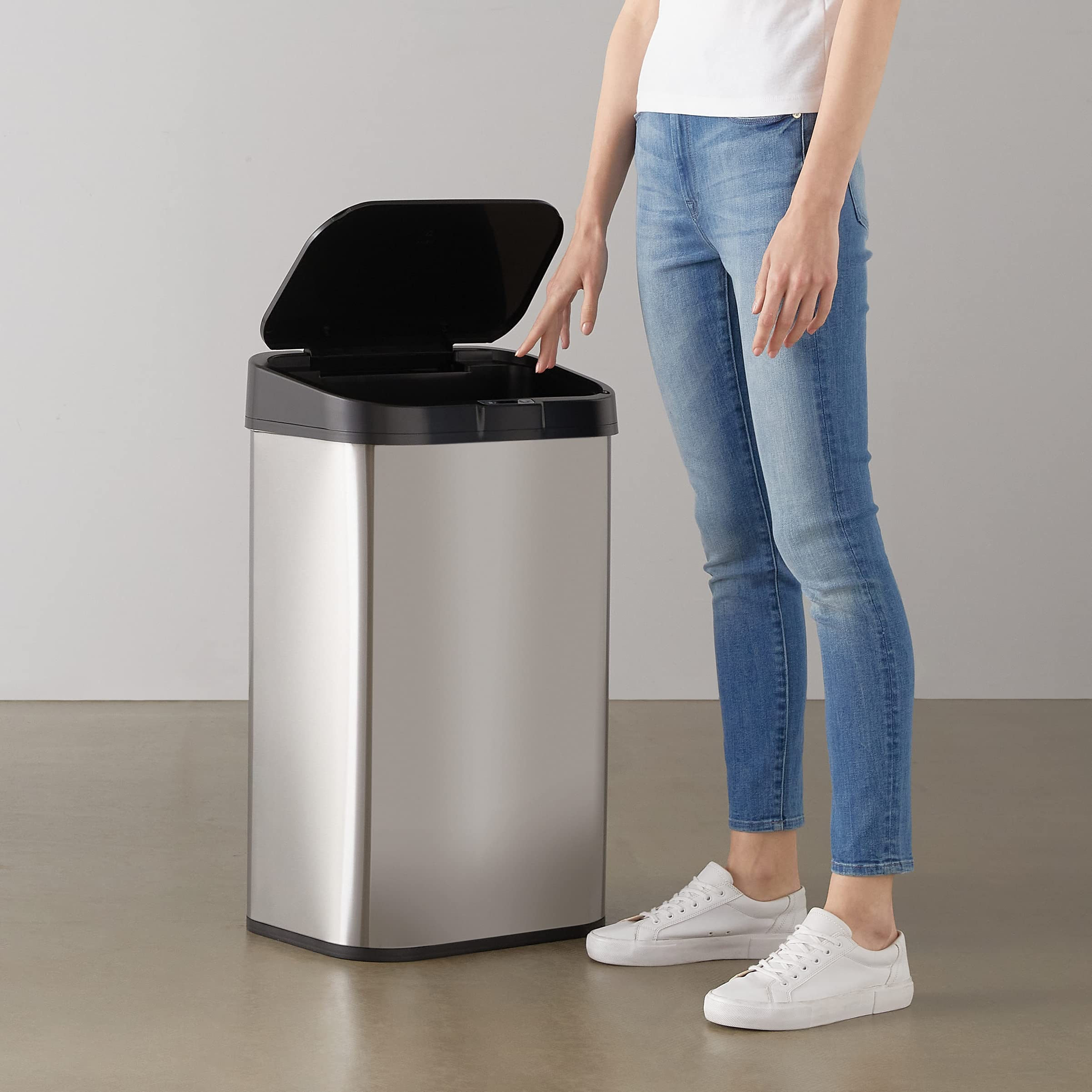 Eine Frau in Jeans und weißem Shirt steht neben einem offenen Edelstahl-Mülleimer.