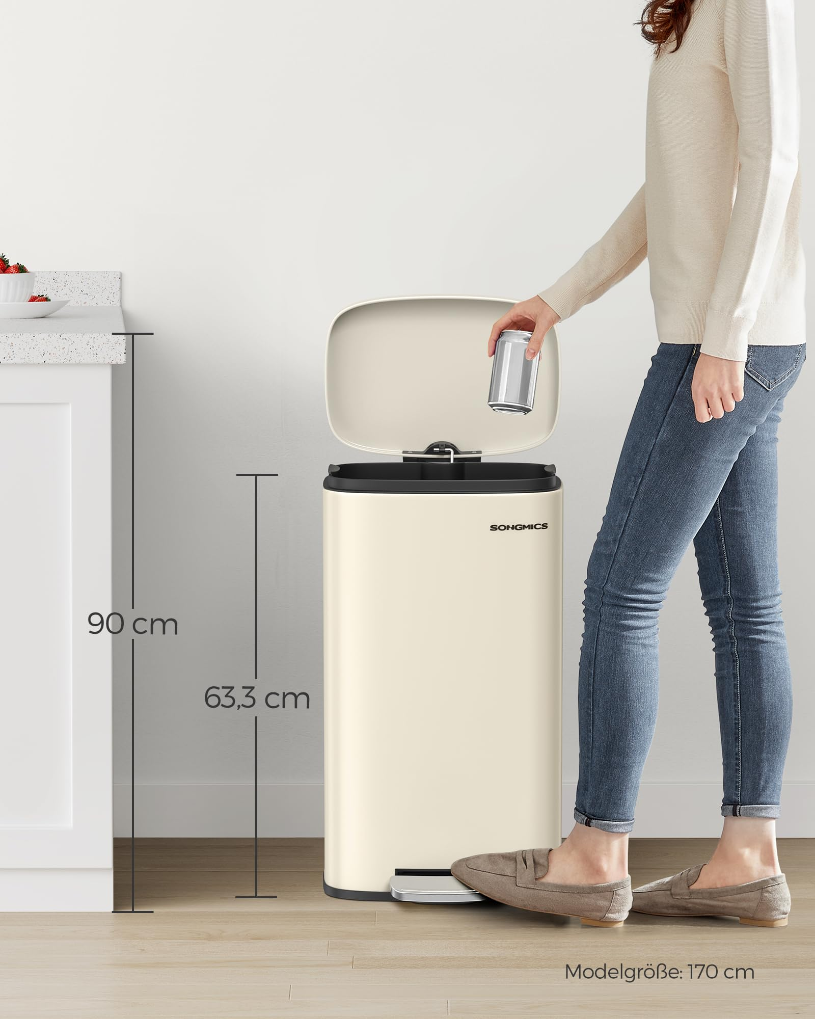 Eine Frau wirft eine Dose in einen beigen Songmics-Treteimer in einer Küche, Maßangaben 90 cm und 63,3 cm.