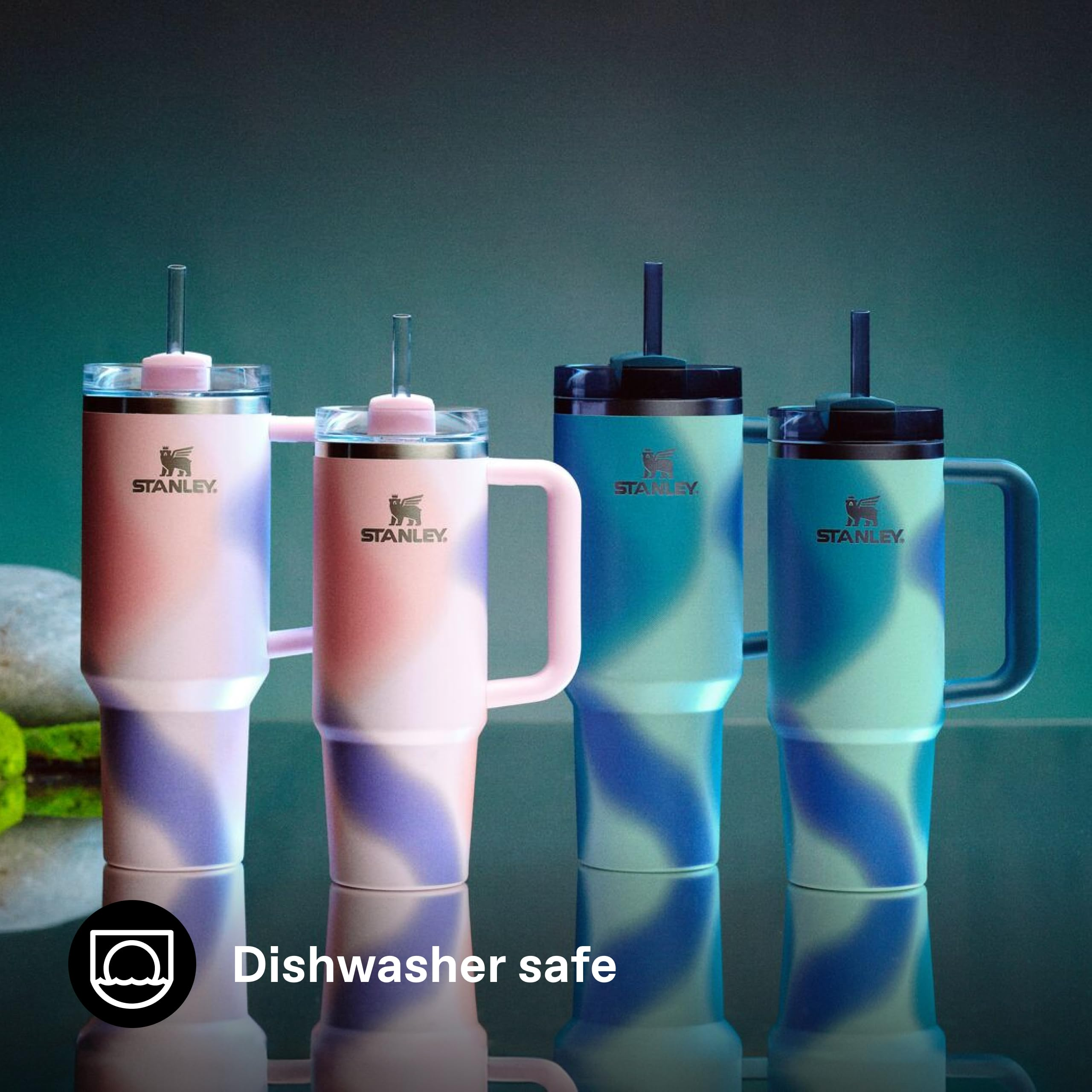 Vier Stanley-Becher mit Henkel und Strohhalm in Rosa-Lila und Blau-Tönen stehen auf einer spiegelnden Fläche.