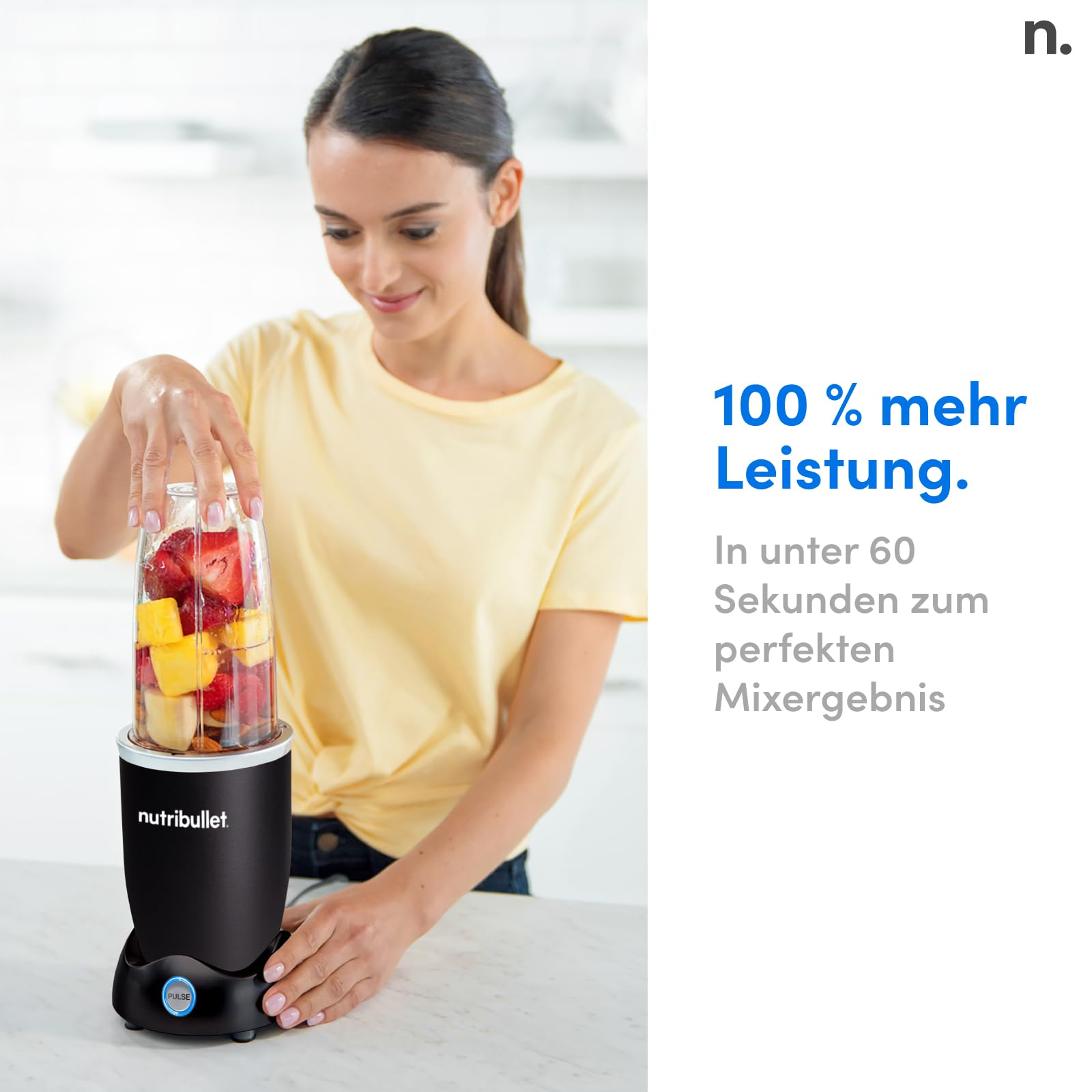 Une femme en chemise jaune prépare un mixeur Nutribullet rempli de fruits.